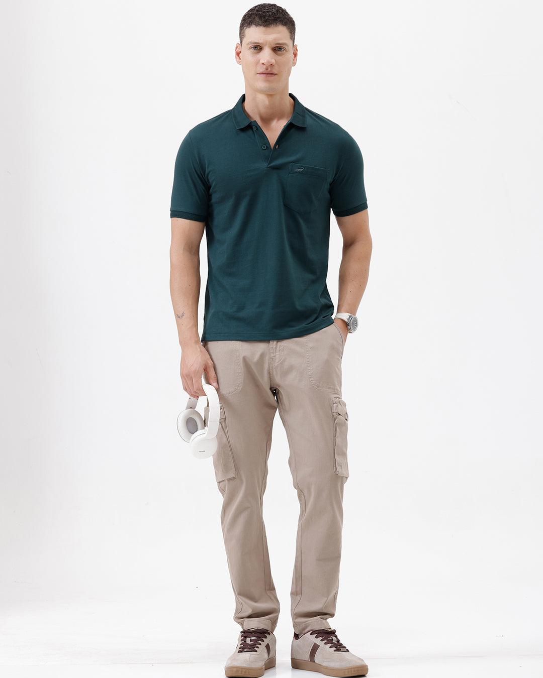 A man wearing a dark teal short-sleeve polo shirt with a chest pocket, paired with beige cargo pants, standing against a plain white studio background.
