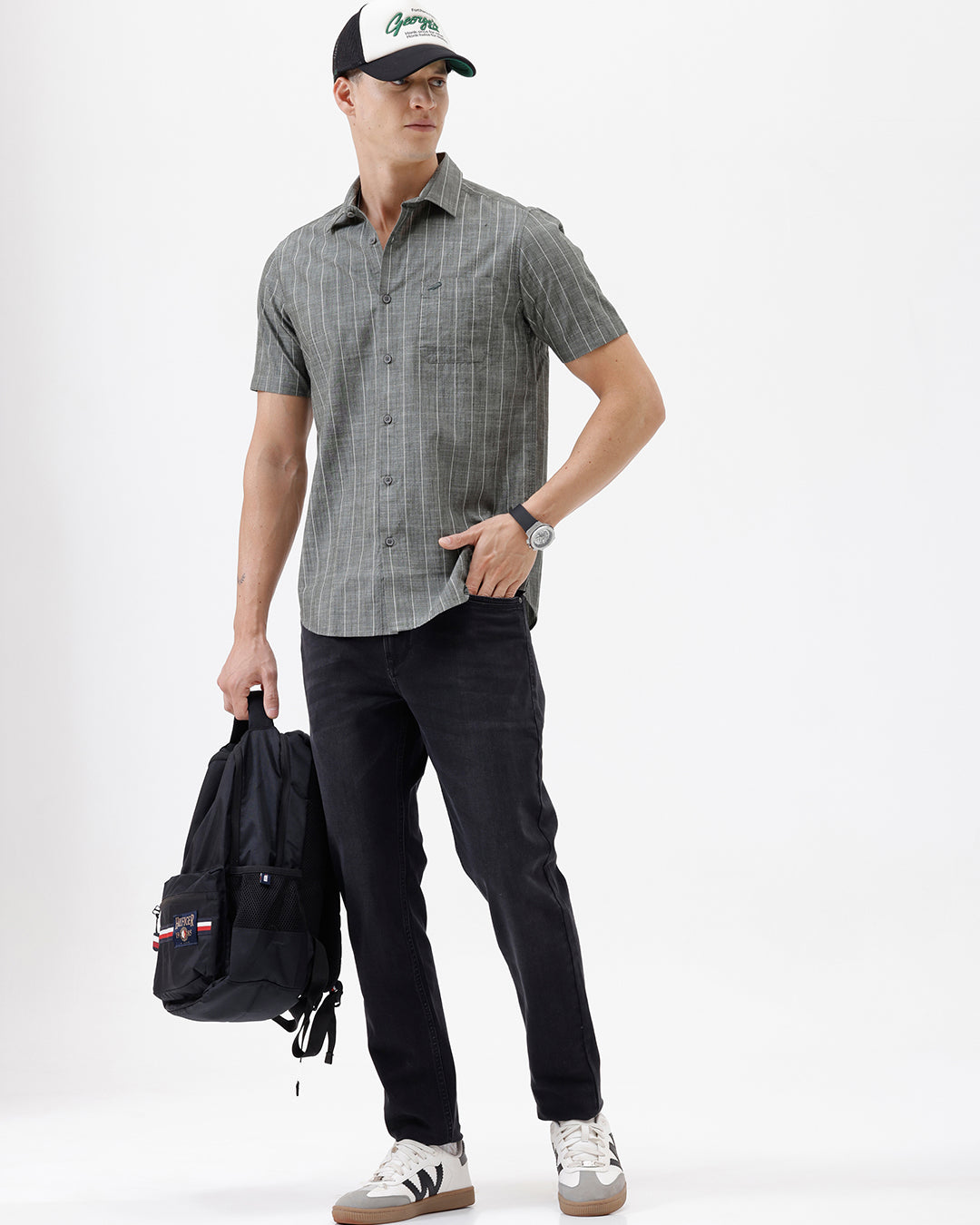 A man wearing a short-sleeve button-up shirt with a gray and white vertical stripe pattern, paired with black pants, standing against a plain white studio background.