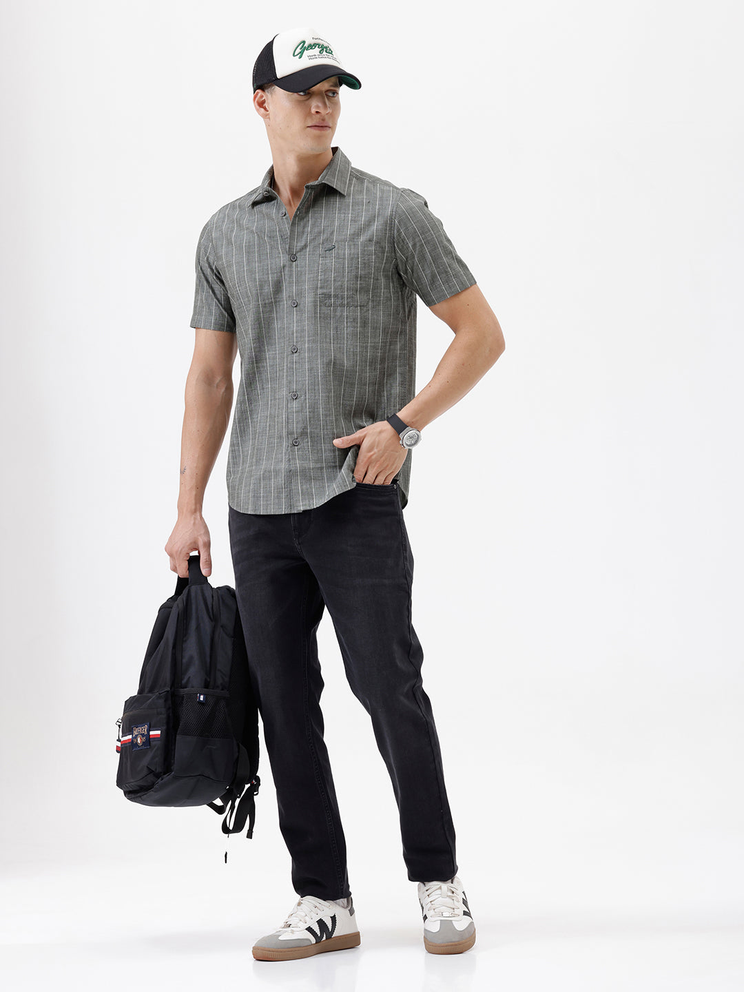 A man wearing a short-sleeve button-up shirt with a gray and white vertical stripe pattern, paired with black pants, standing against a plain white studio background.