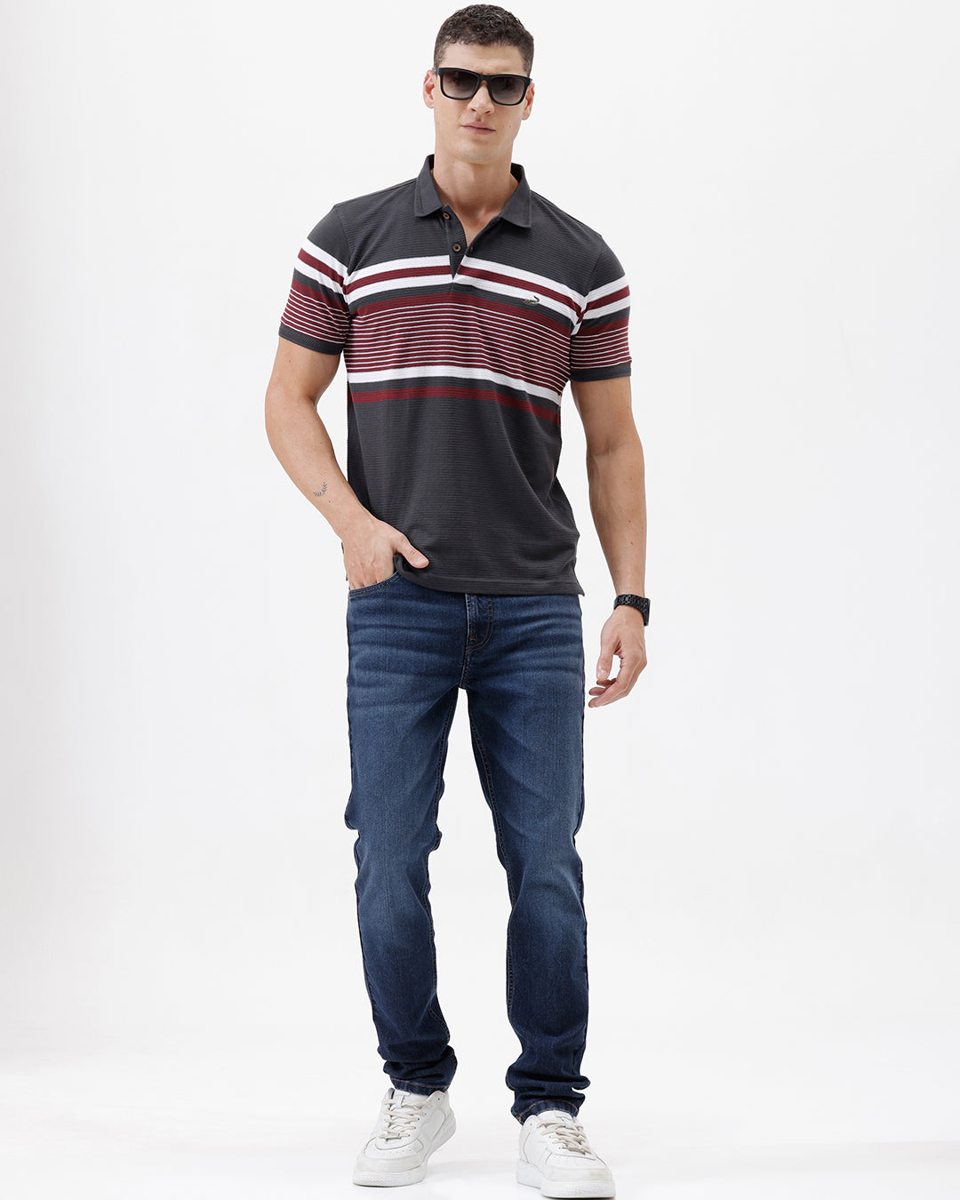 A person wearing dark blue slim-fit jeans with a faded wash, paired with a black t-shirt and white sneakers, shown from the waist down against a plain white studio background.