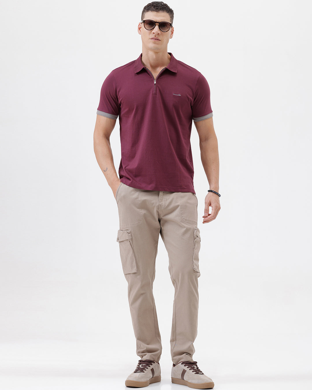 A man wearing a short-sleeve polo shirt in maroon with gray sleeve trim and a half-zip collar, paired with beige cargo pants, against a plain white studio background.