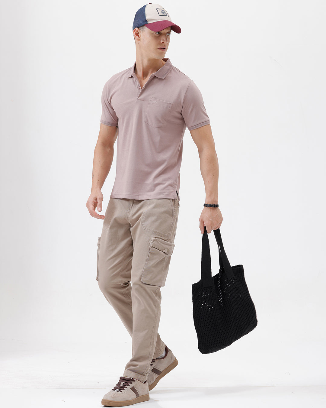 A man modeling a short-sleeve polo shirt in a dusty mauve-pink color, paired with khaki cargo pants and a baseball cap, against a plain light gray background.