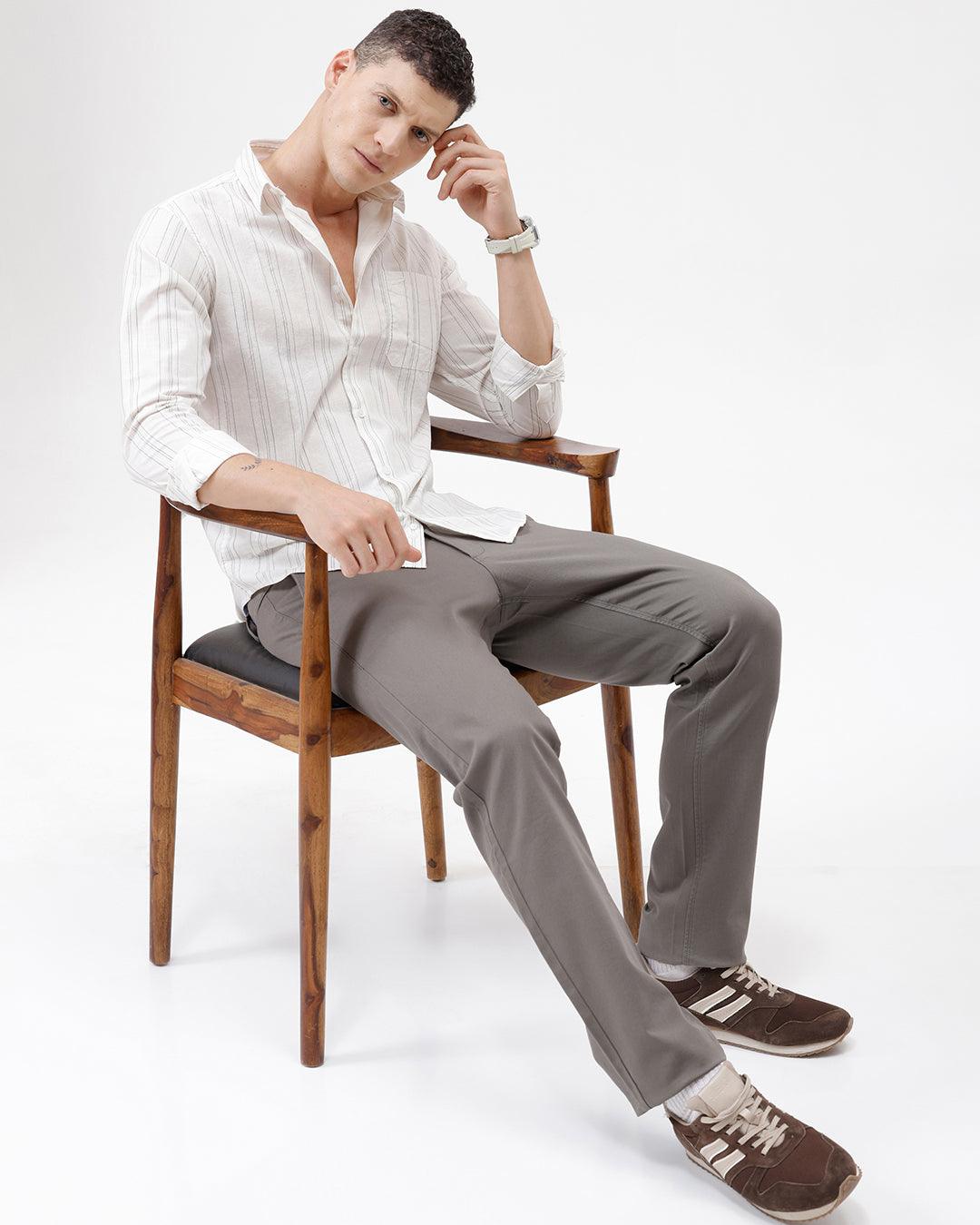 A man wearing a white long-sleeve button-up shirt with thin vertical gray stripes and black pants, standing against a plain white studio background.