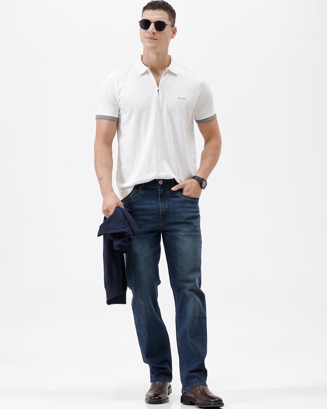 A man wearing a white short-sleeve polo shirt with gray ribbed trim on the collar and sleeve cuffs, paired with dark blue jeans, photographed against a plain white studio background.