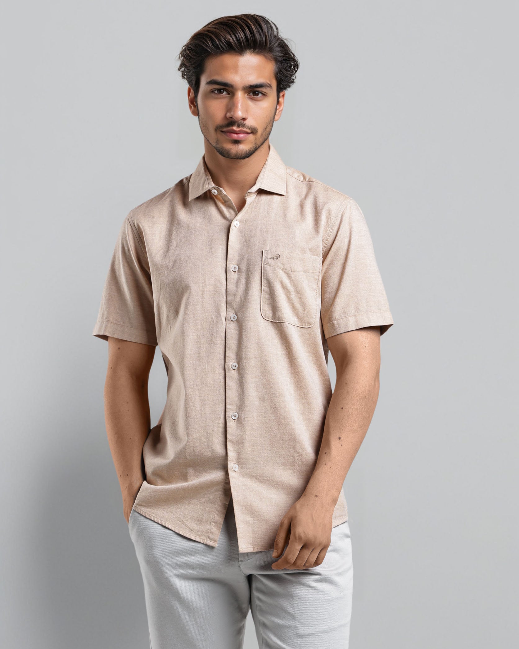 Man wearing a beige shirt and light gray pants against a plain background