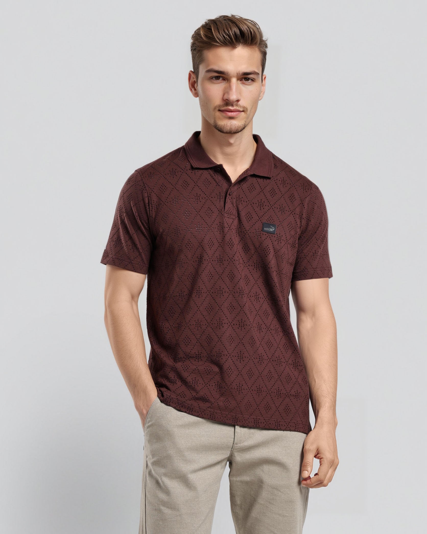 Man wearing a maroon patterned polo shirt and beige pants on a light gray background