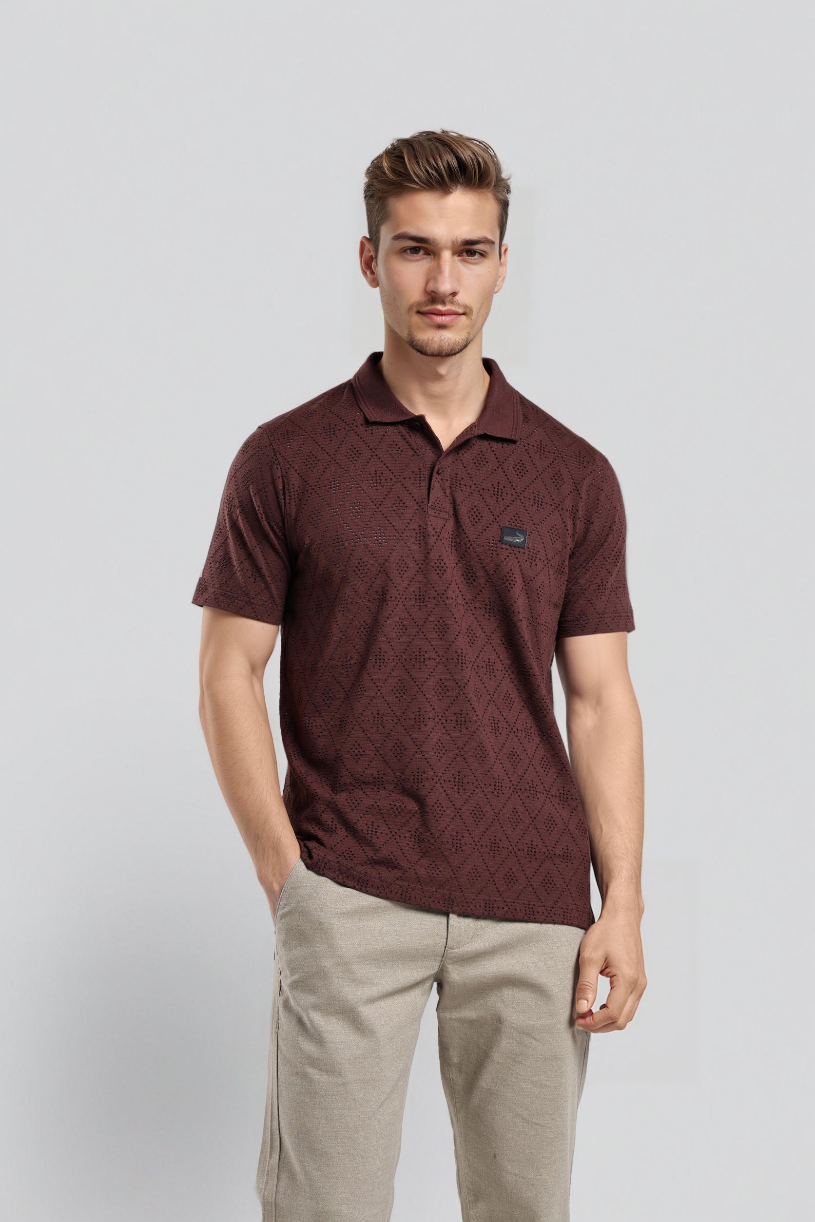 Man wearing a maroon patterned polo shirt and beige pants on a light gray background