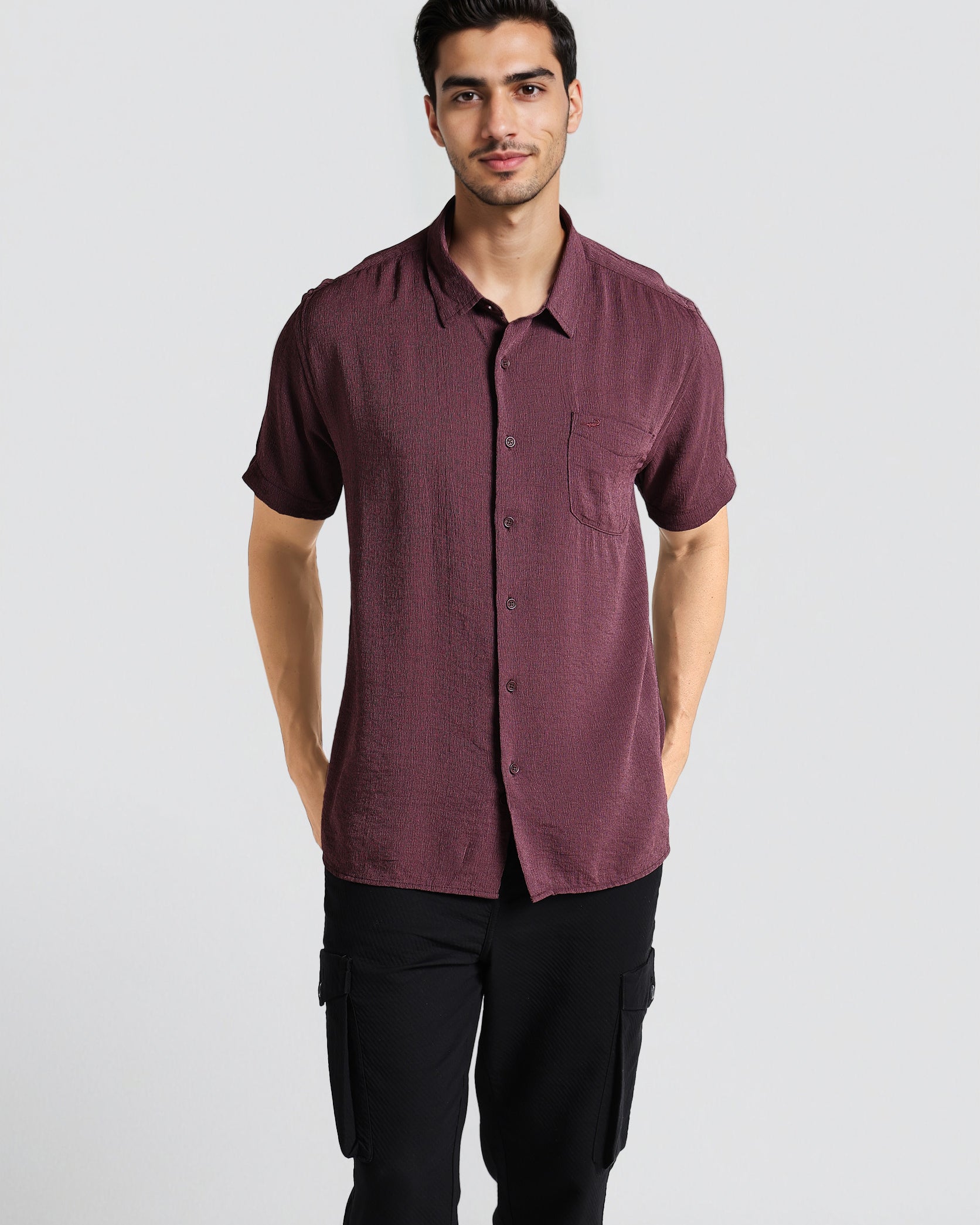 Man wearing a maroon button-up shirt and black pants on a light gray background