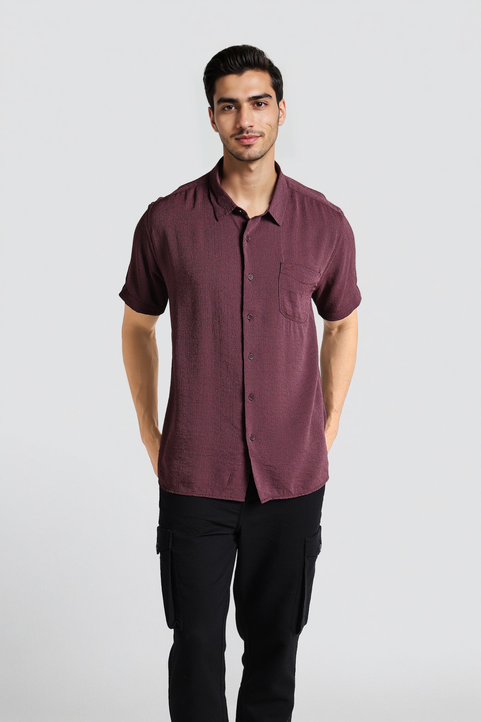 Man wearing a maroon button-up shirt and black pants on a light gray background