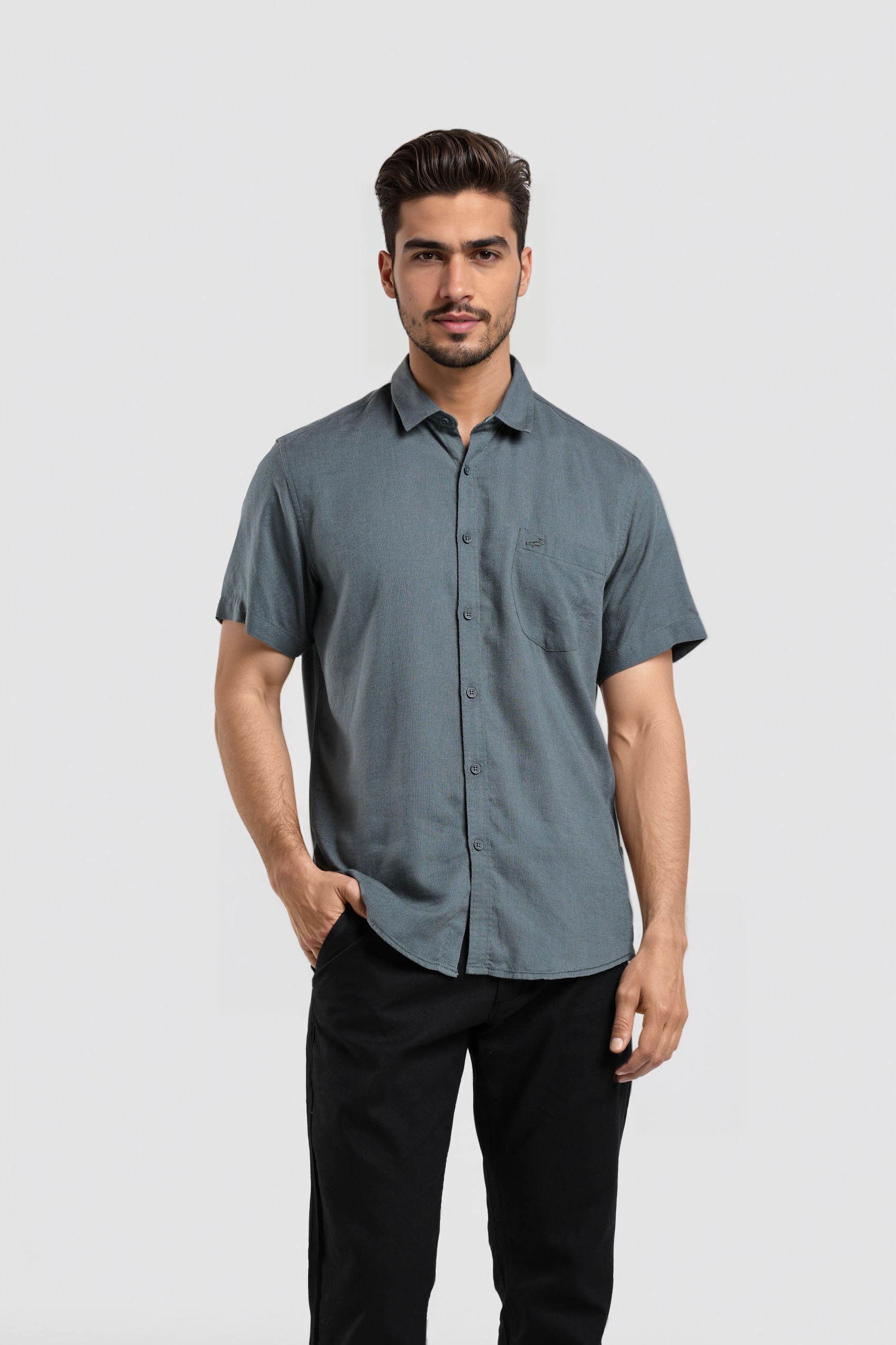 Man wearing a gray button-up shirt and black pants on a light gray background