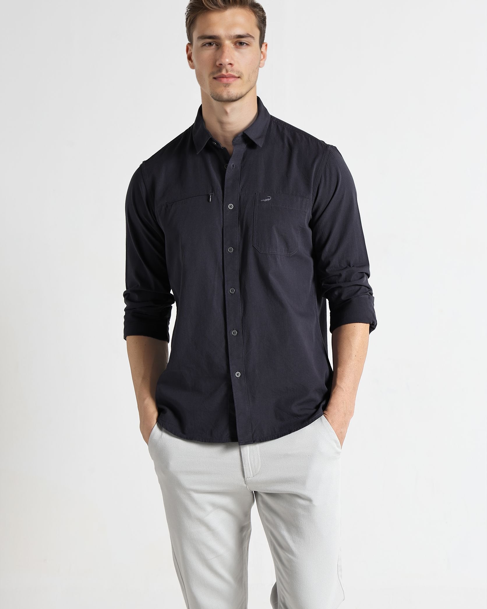 Man wearing a dark blue button-up shirt and light gray pants on a white background