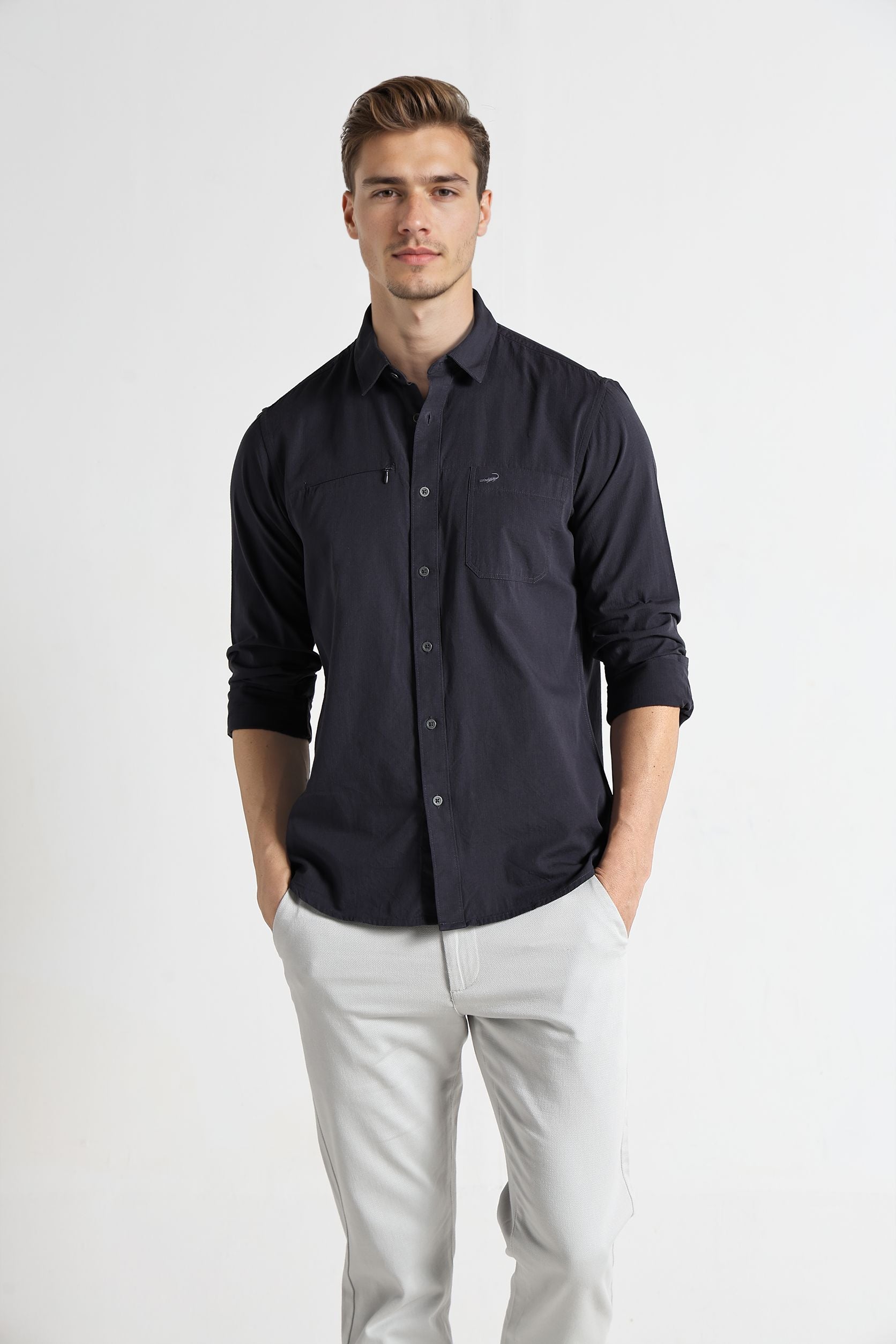 Man wearing a dark blue button-up shirt and light gray pants on a white background