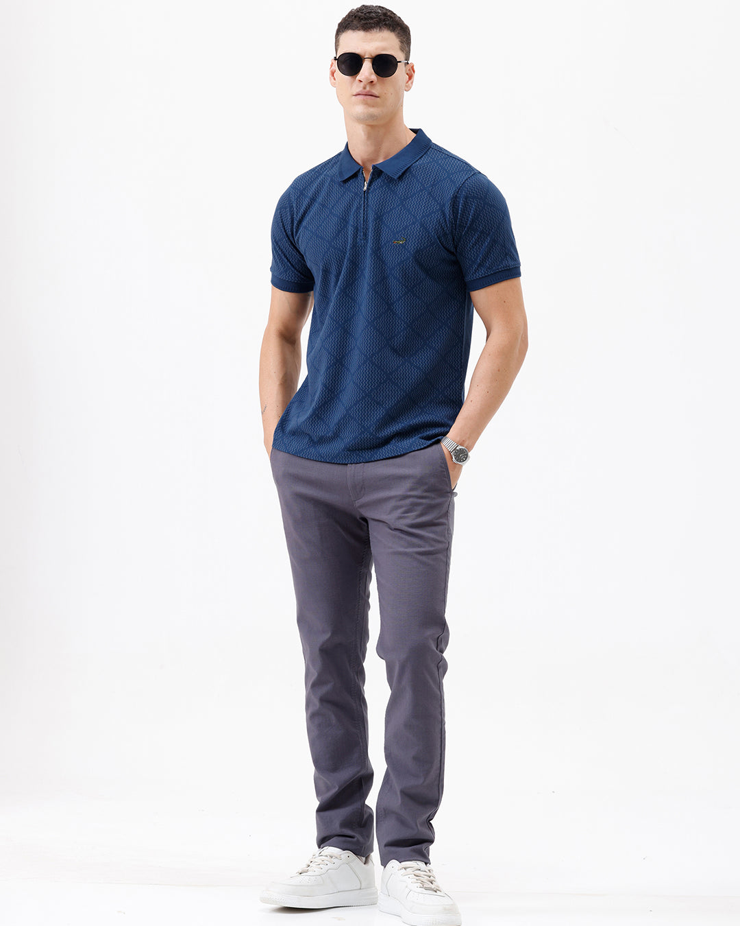 A man wearing a navy blue short-sleeve polo shirt with a subtle geometric pattern and a half-zip collar, paired with gray trousers, against a plain white background.