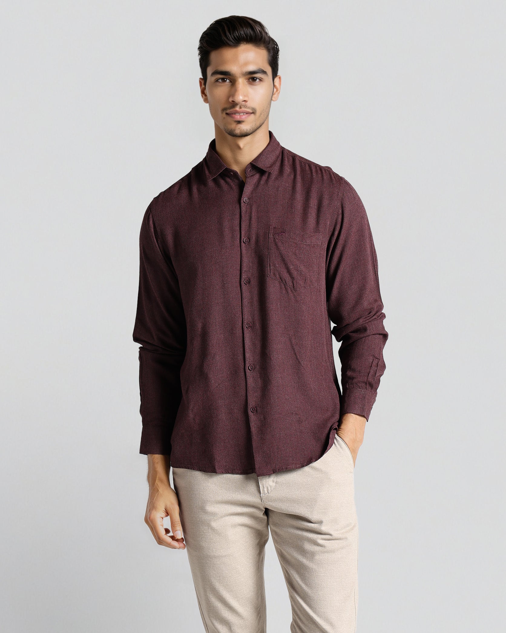 Man wearing a maroon shirt and beige pants on a light gray background