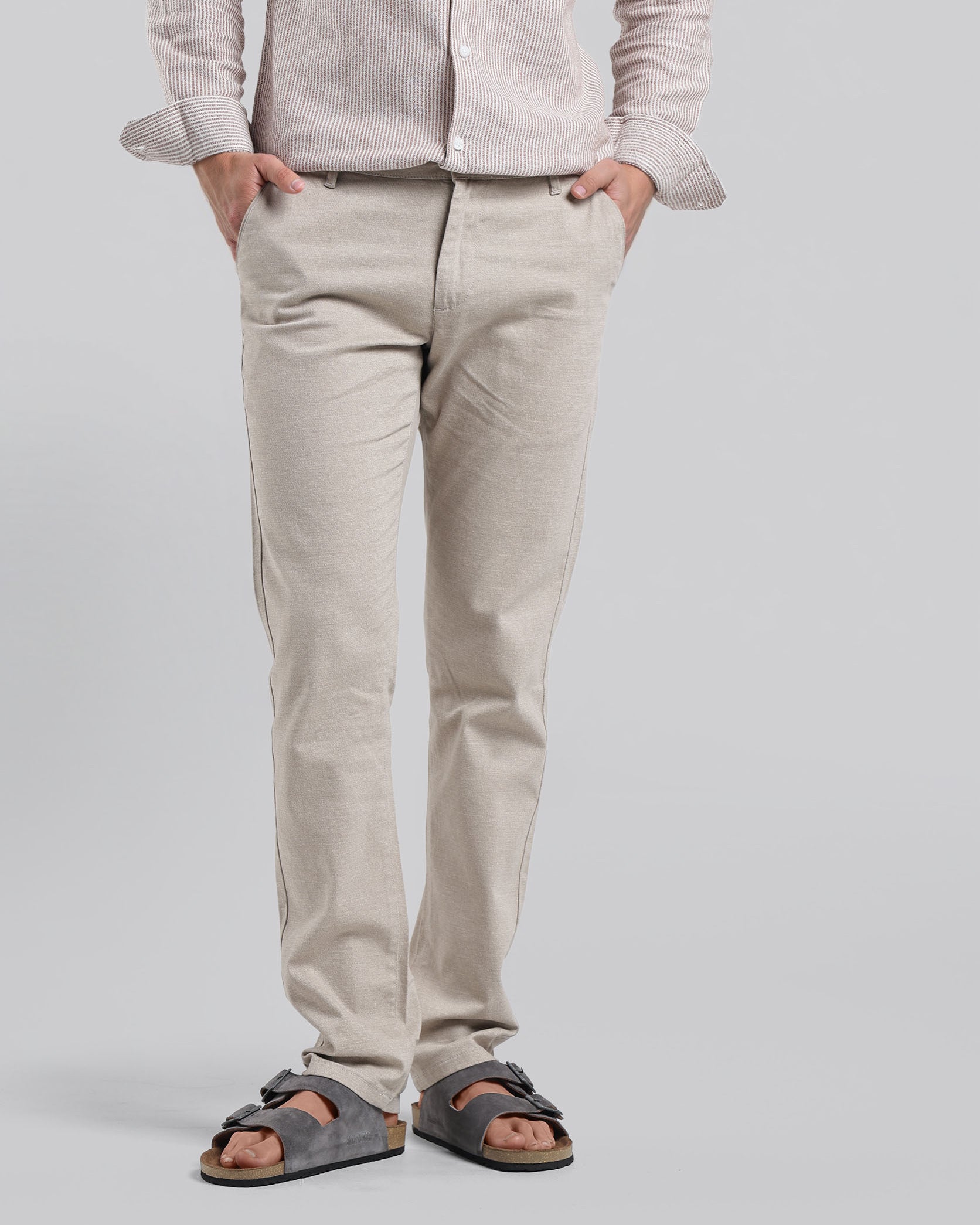 Person wearing a light-colored shirt and pants with sandals on a plain background