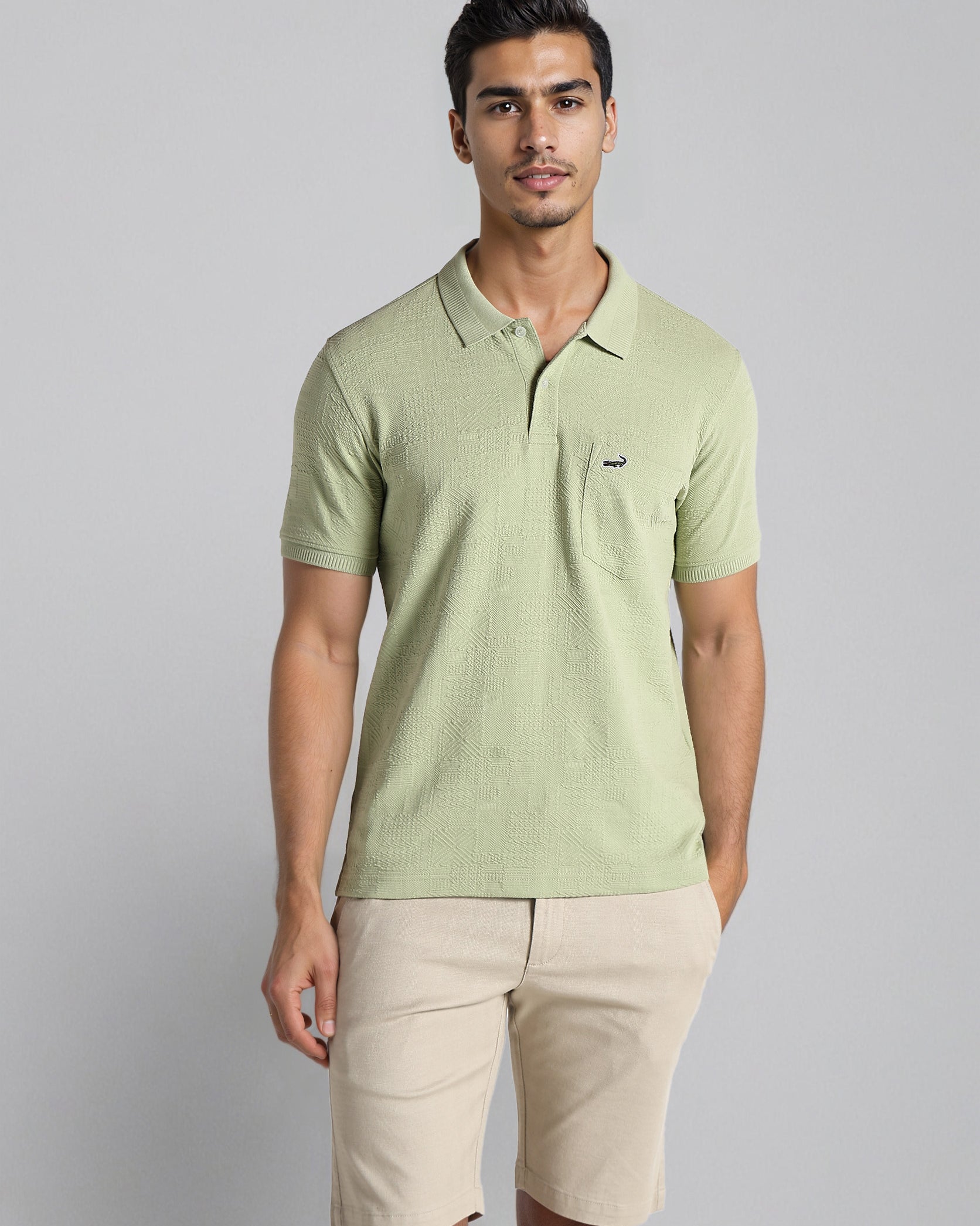Man wearing a light green polo shirt and beige shorts on a gray background