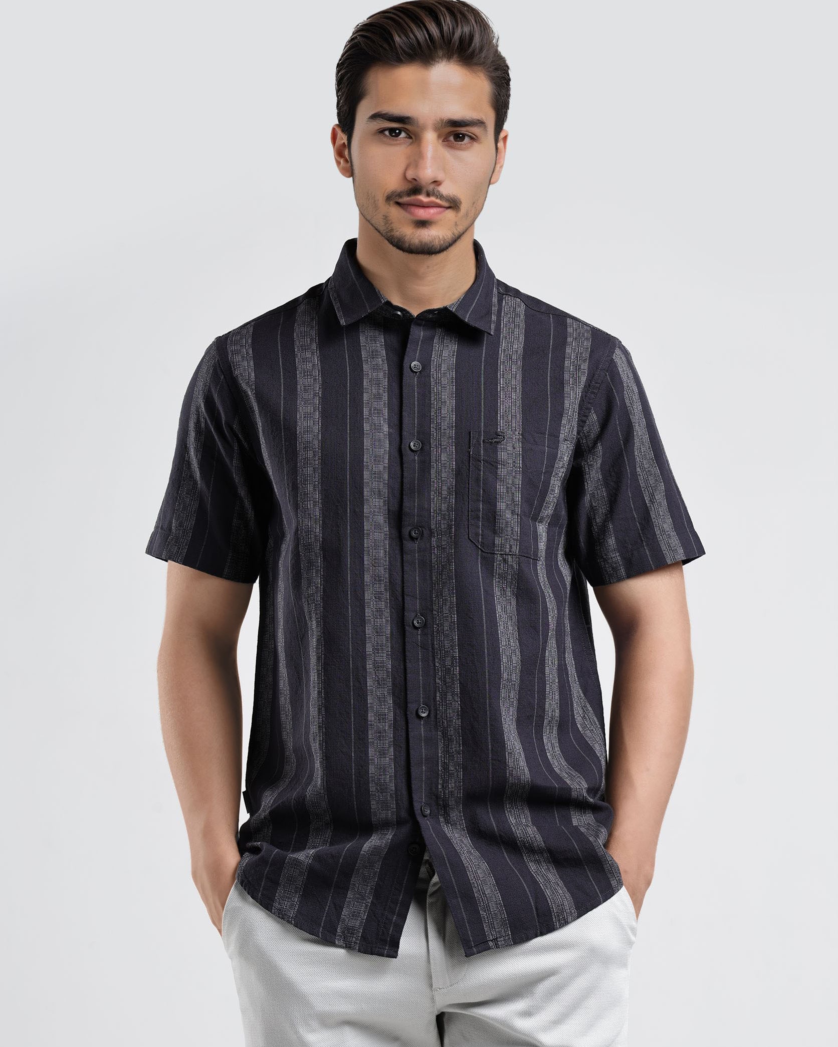 Man wearing a dark patterned shirt and light pants on a white background