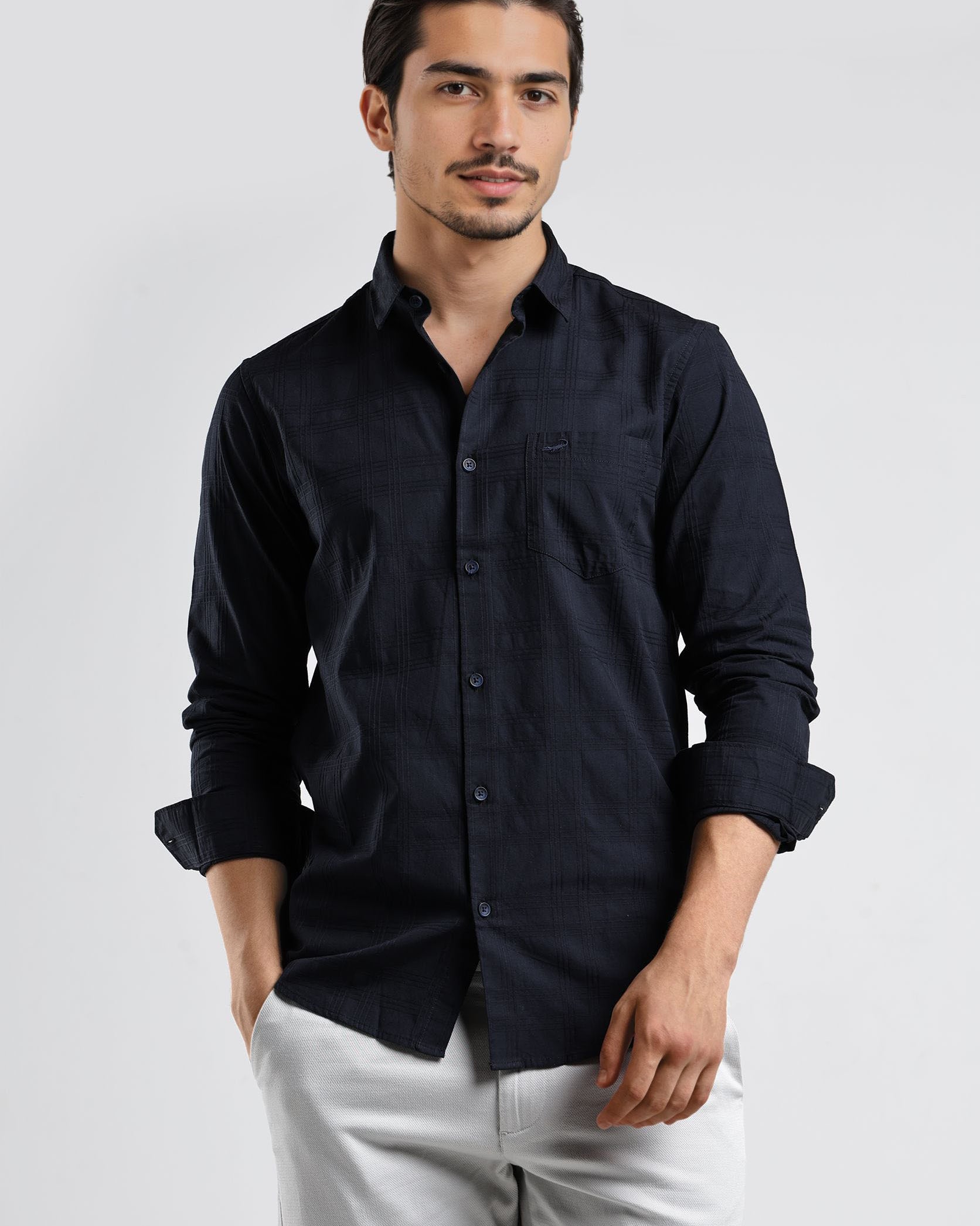 Man wearing a black button-up shirt and white pants on a light gray background