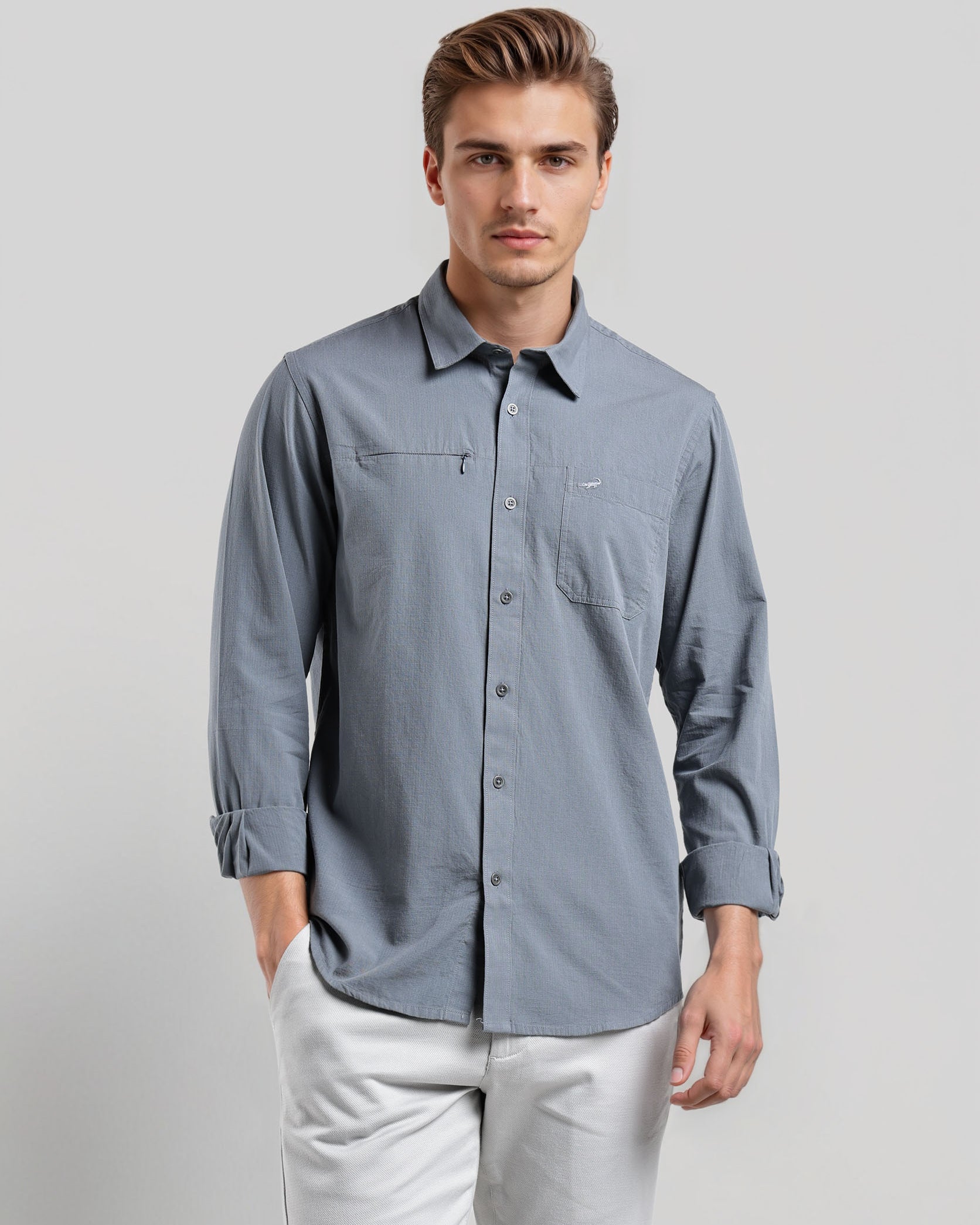 Man wearing a light blue button-up shirt and white pants on a gray background