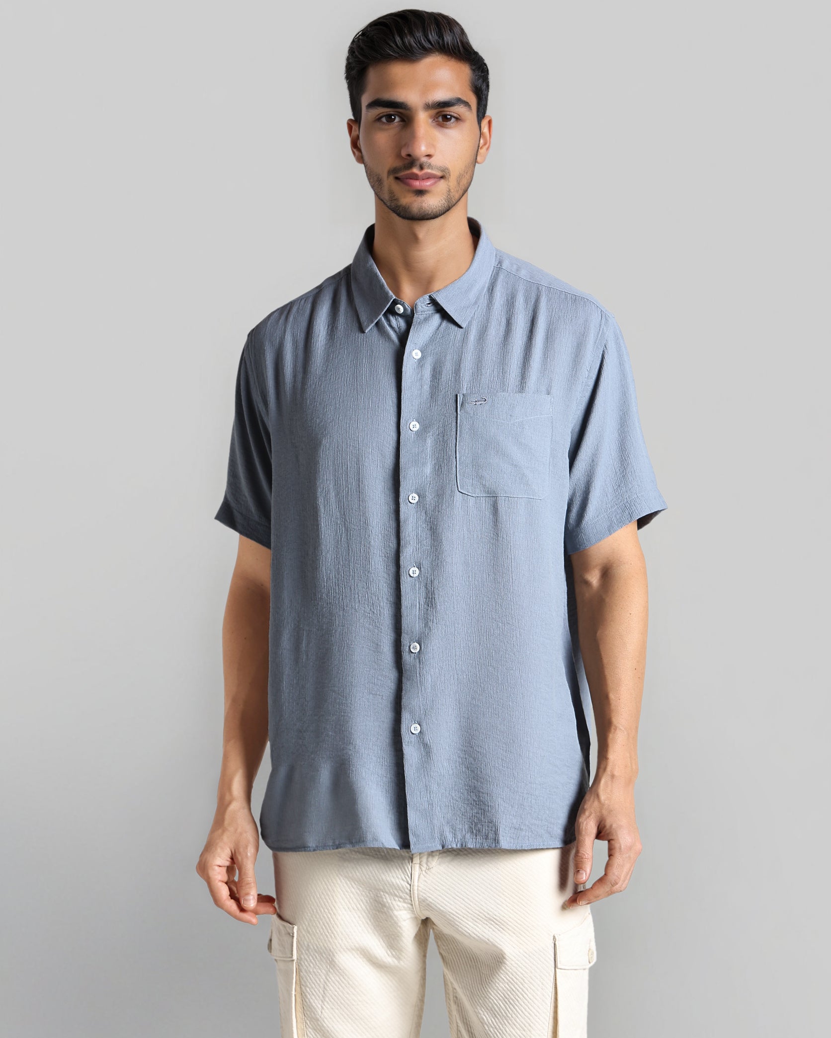 Man wearing a light blue short-sleeve shirt and beige pants against a gray background