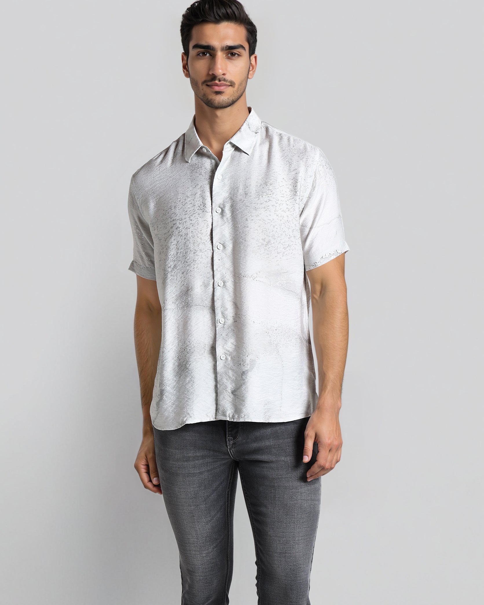 Man wearing a light gray patterned shirt and dark gray jeans on a white background