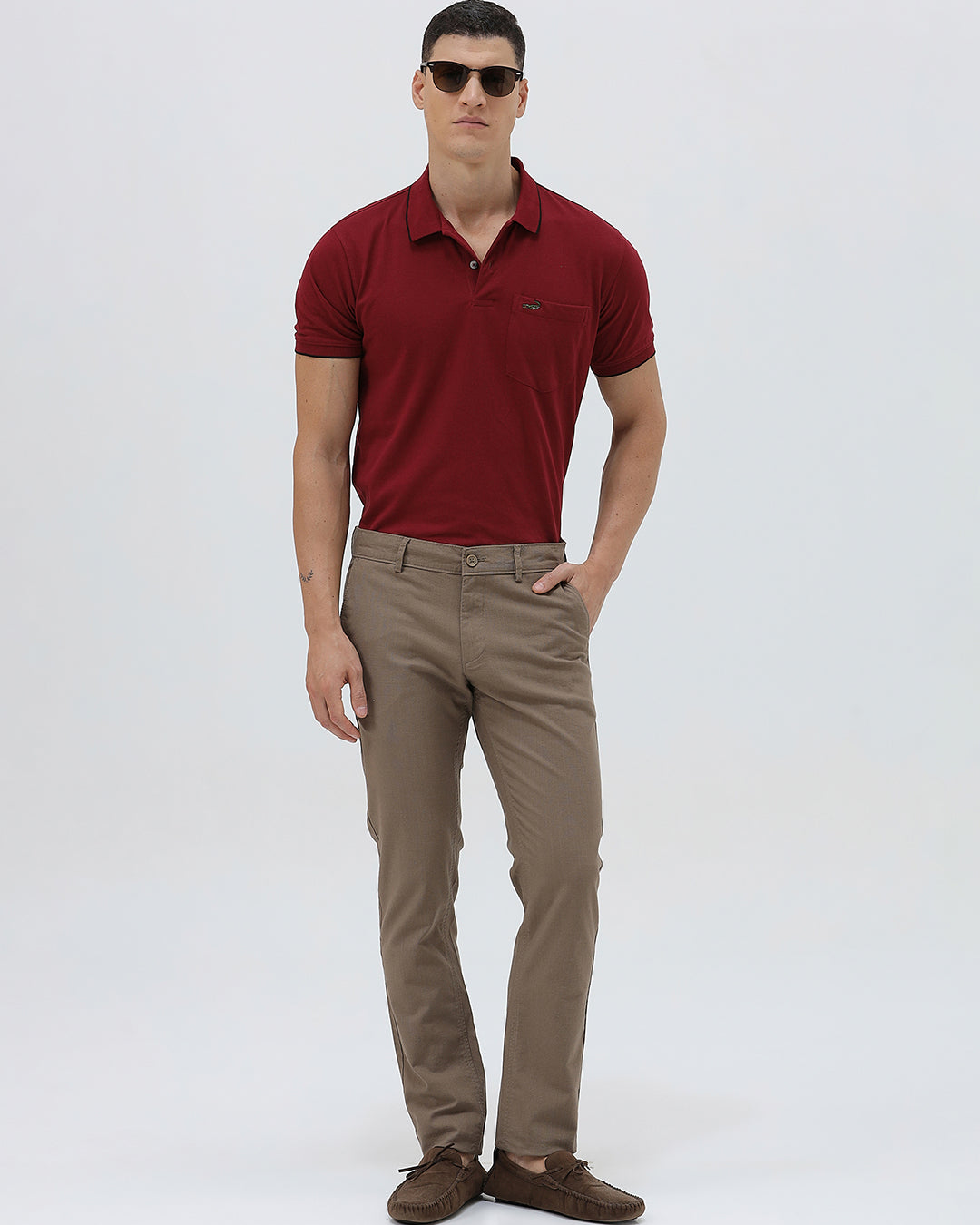 A person wearing slim-fit brown trousers, paired with a dark red shirt and brown suede moccasin shoes, shown from the waist down against a plain white studio background.