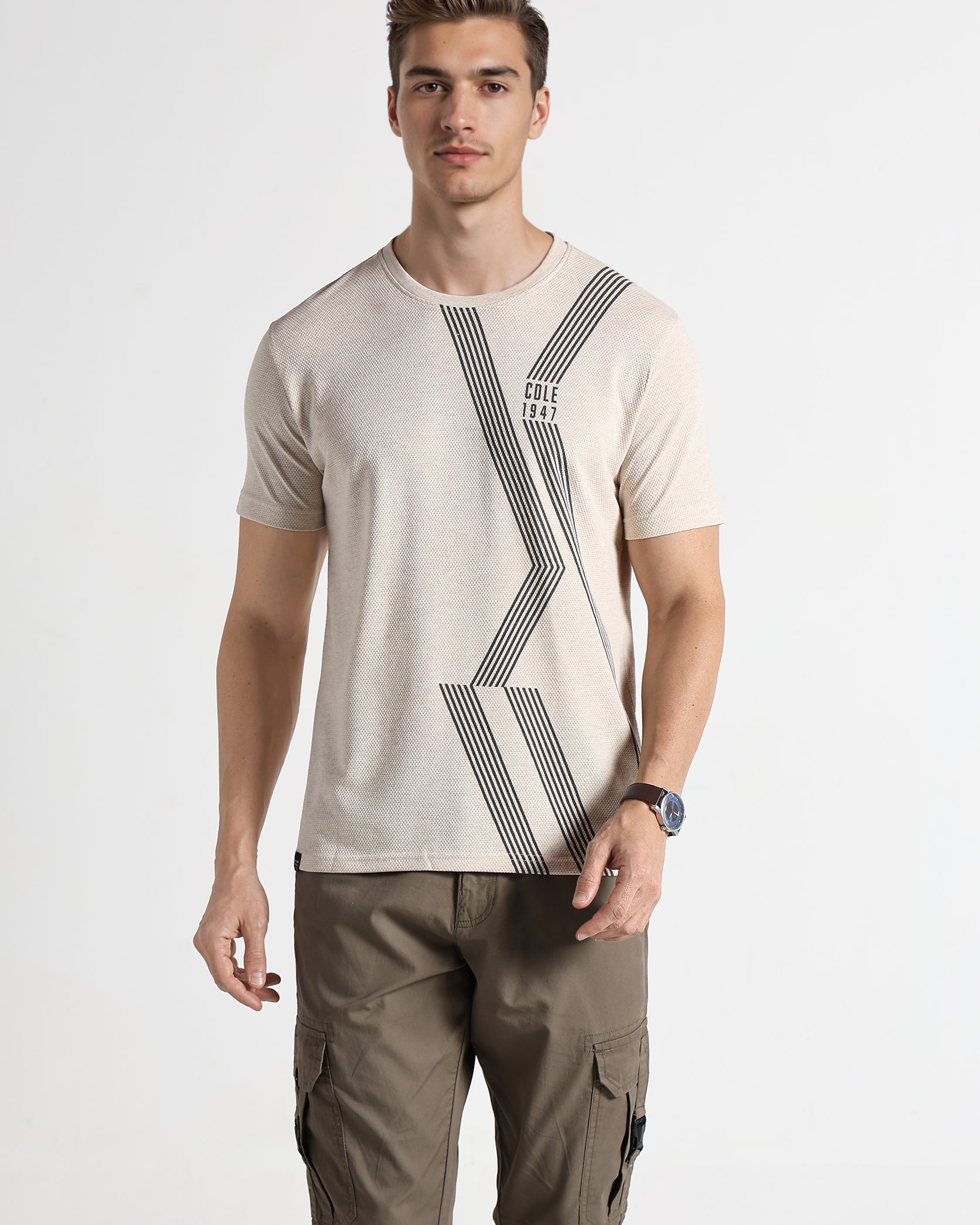 Man wearing a beige t-shirt with a geometric design and brown cargo pants on a white background