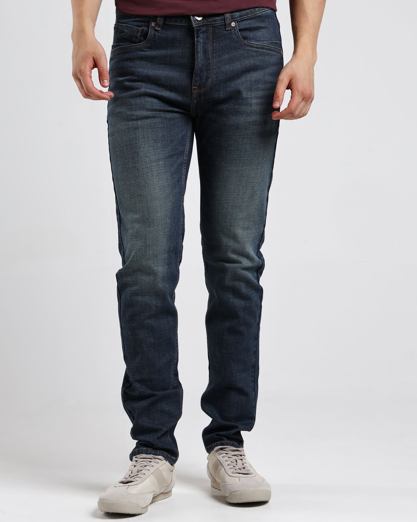 Person wearing dark blue jeans and a maroon shirt on a white background