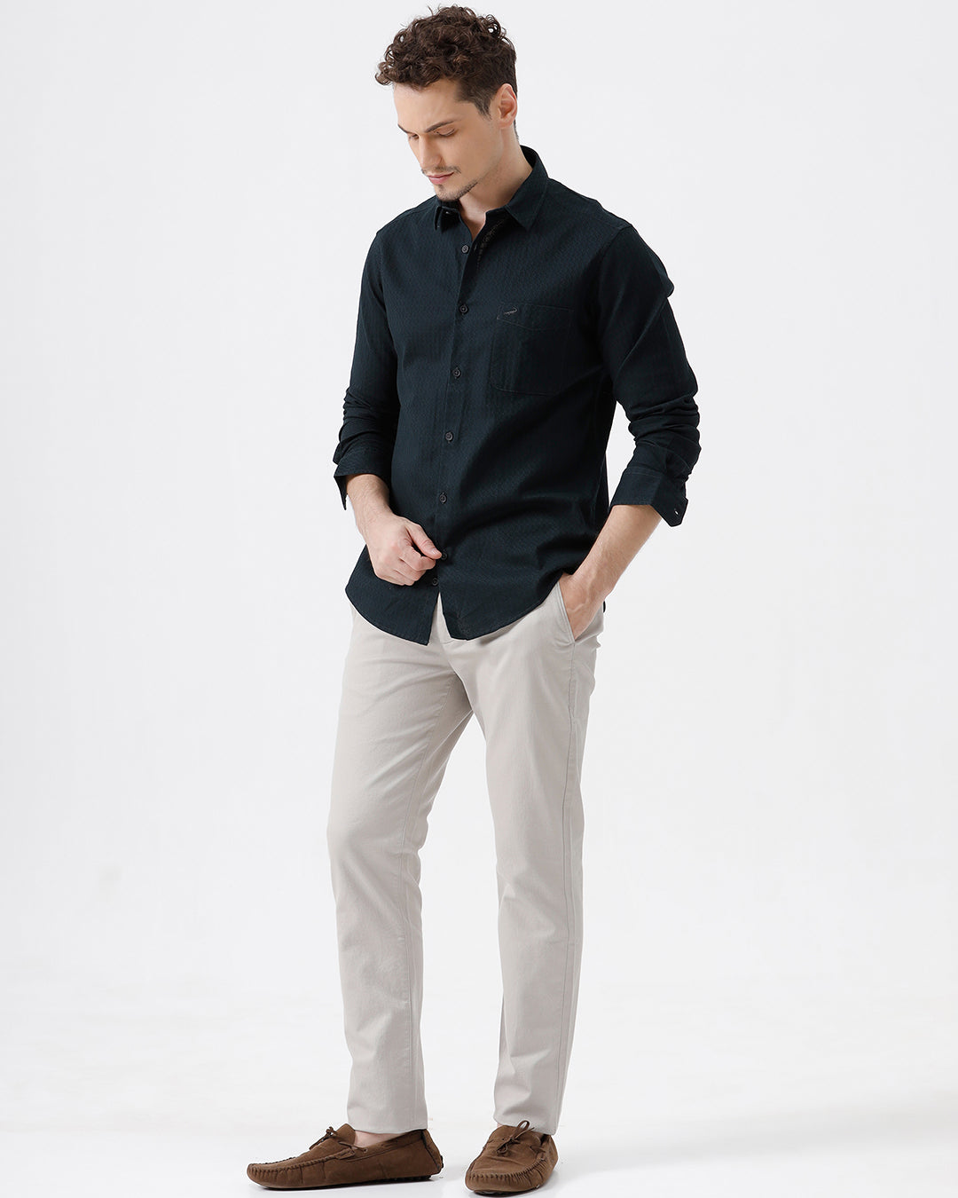 A person wearing slim-fit light beige chino pants, paired with a dark navy long-sleeve button-up shirt and brown suede moccasin-style shoes, photographed against a clean white studio background.