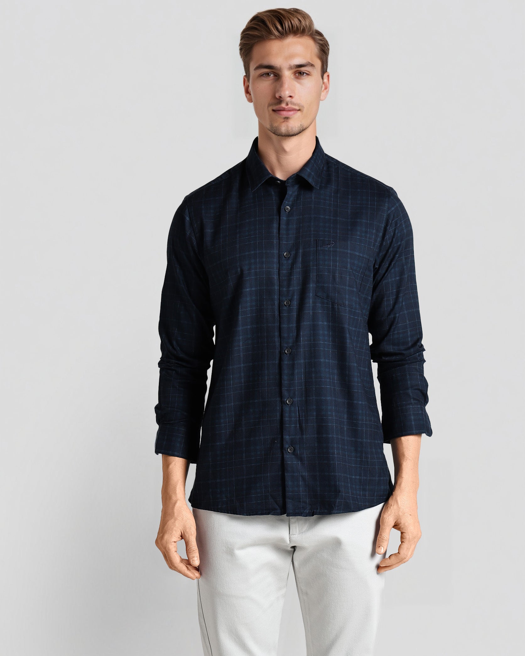 Man wearing a dark blue checkered shirt and white pants on a light gray background