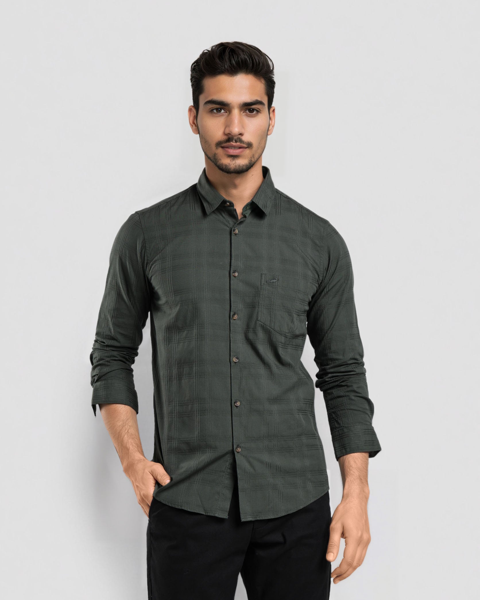 Man wearing a dark green button-up shirt and black pants on a light gray background