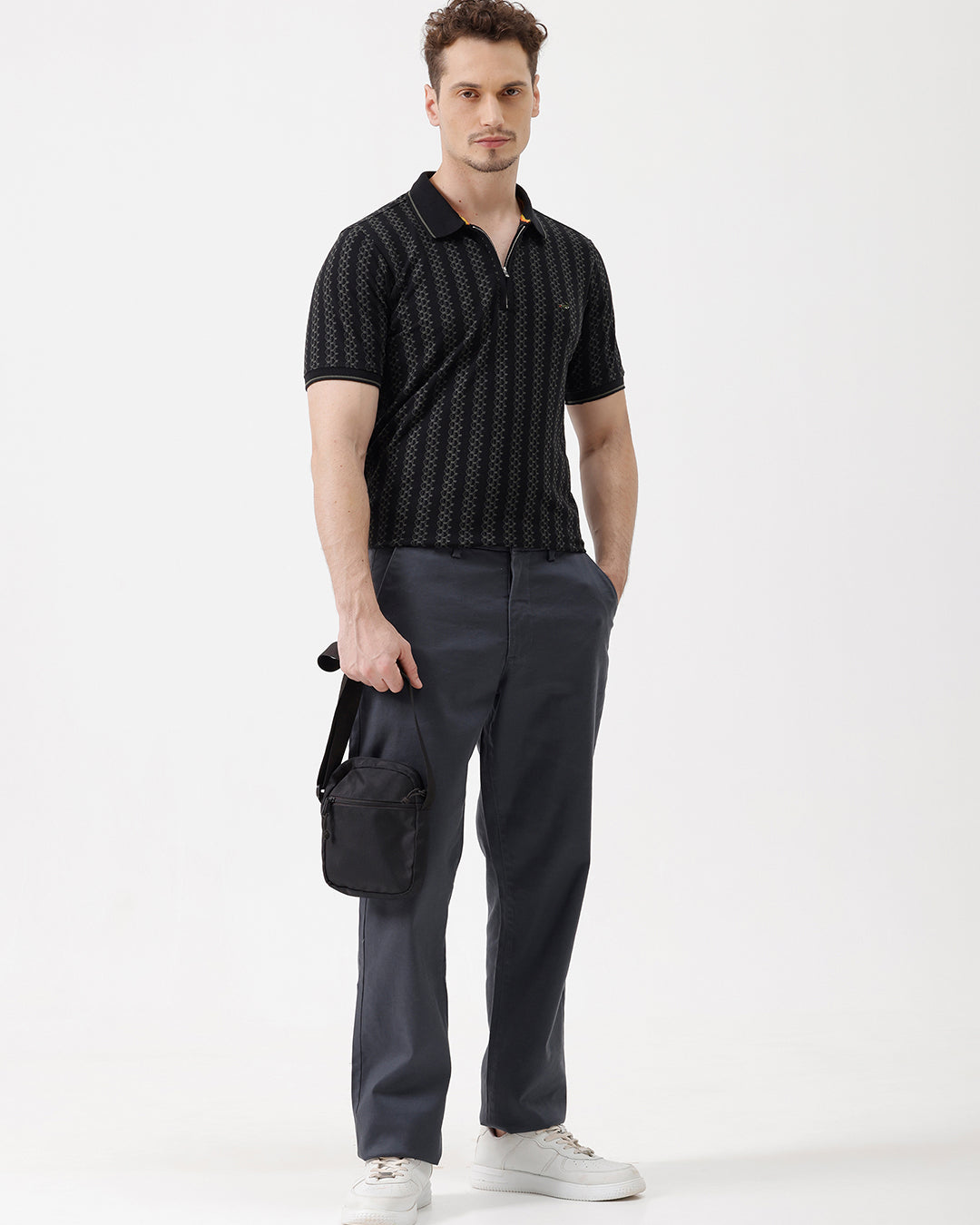 A man wearing a black short-sleeve polo shirt with a subtle geometric pattern, paired with dark gray trousers, standing against a plain white studio background.