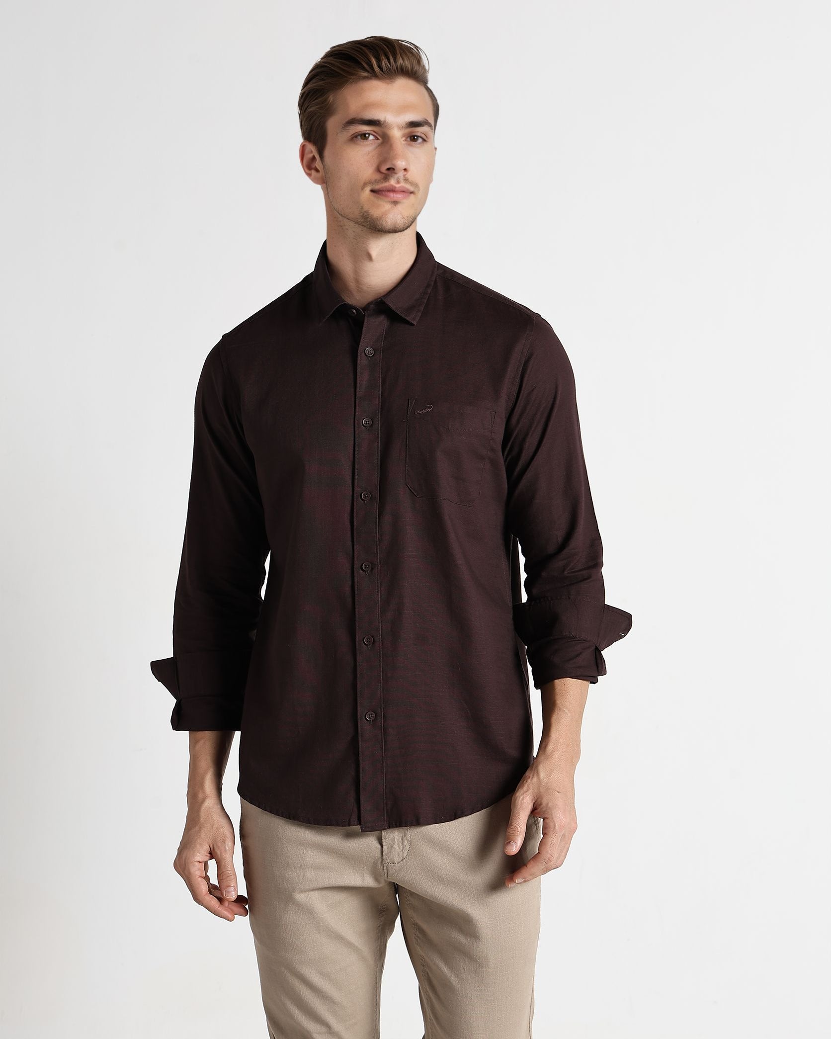 Man wearing a dark brown button-up shirt and beige pants on a white background