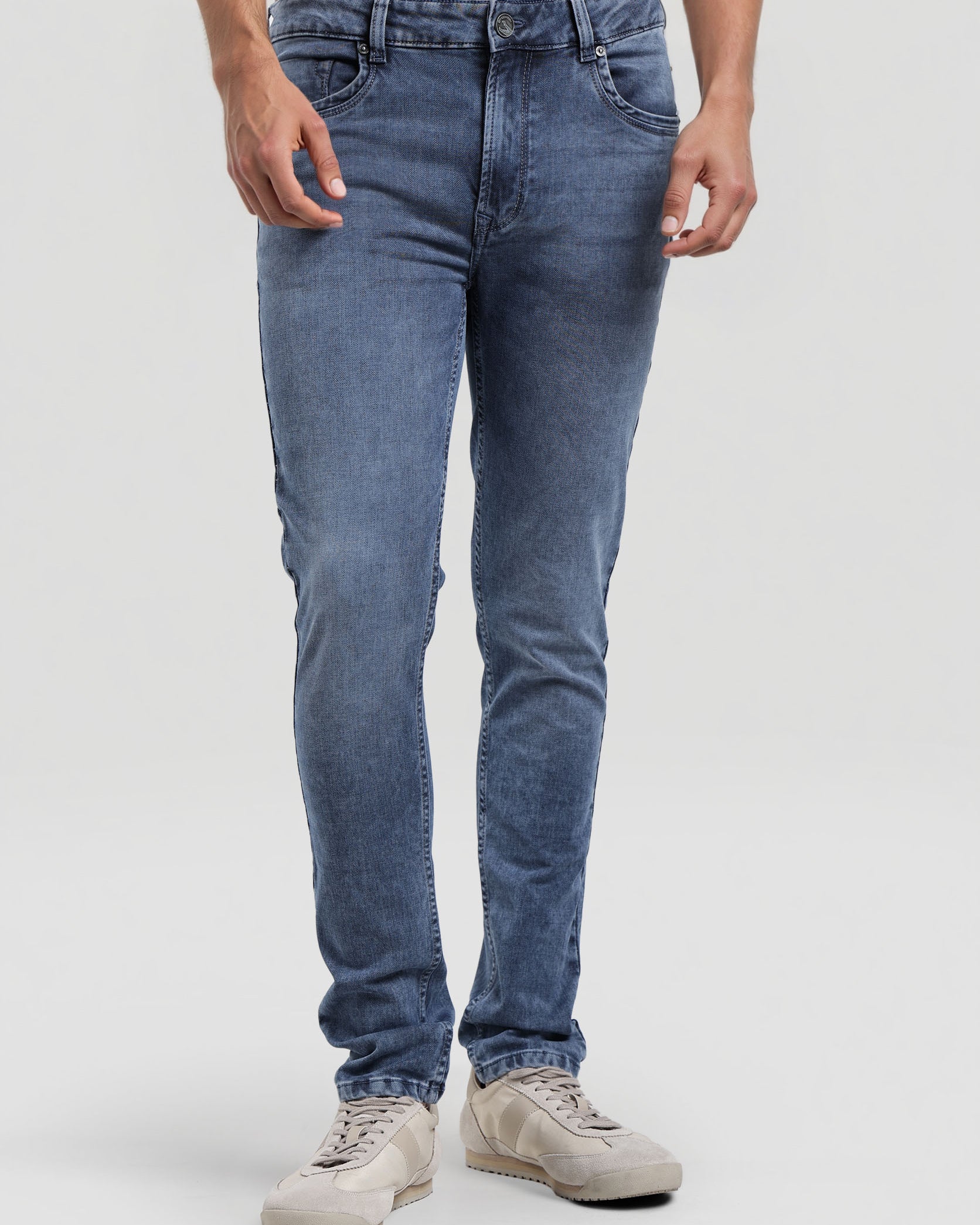 Person wearing blue jeans and beige shoes on a white background