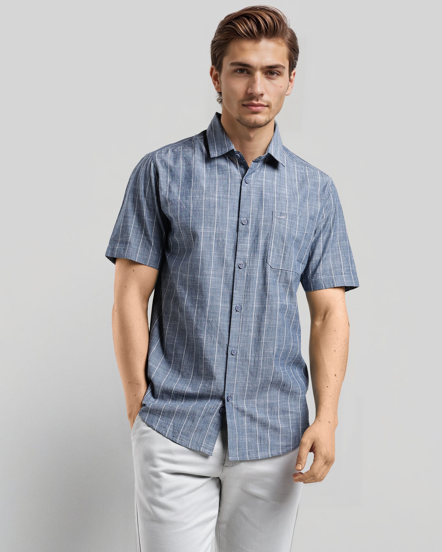 Man wearing a blue checkered shirt and light gray pants against a plain background