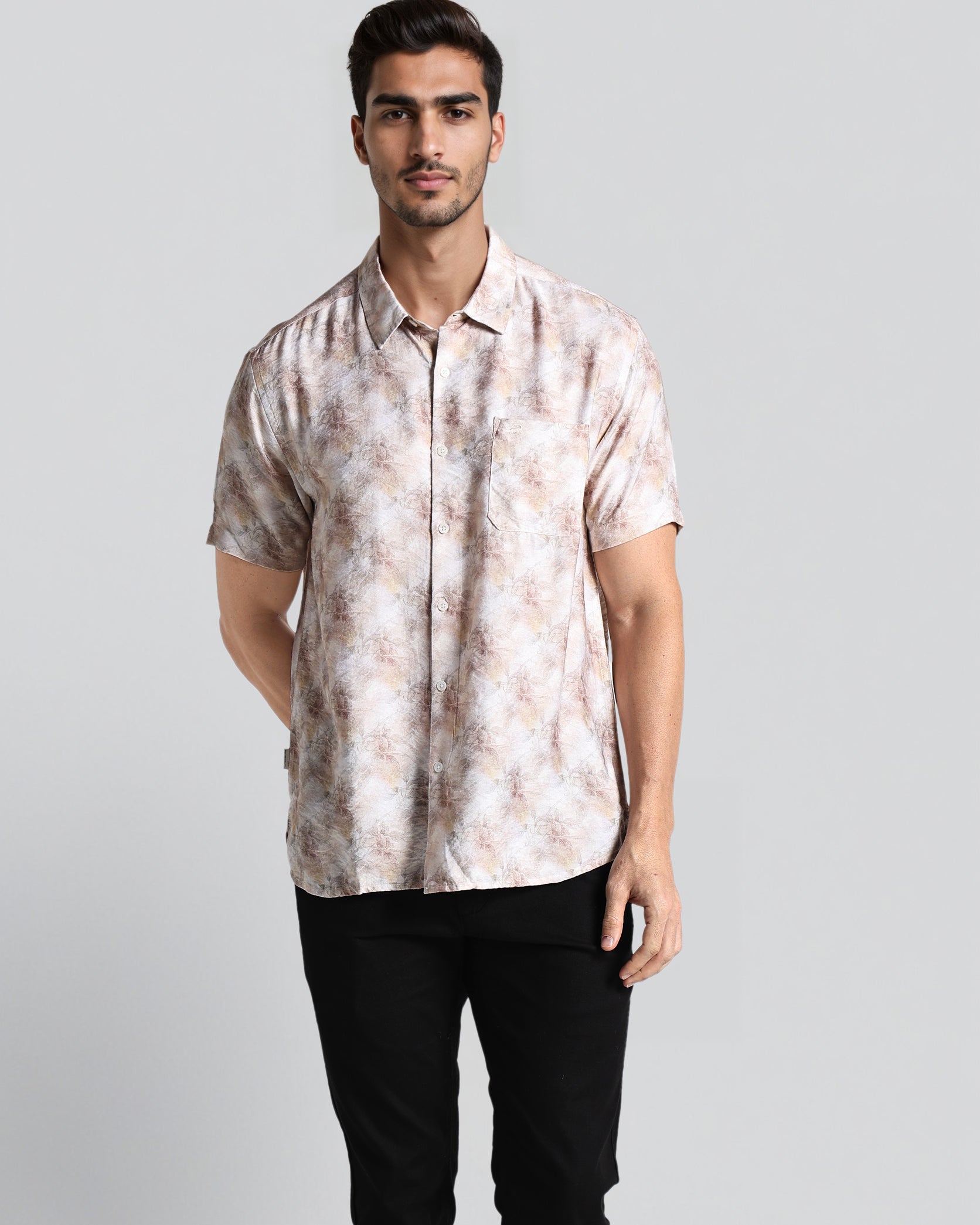 Man wearing a patterned shirt and black pants on a light gray background