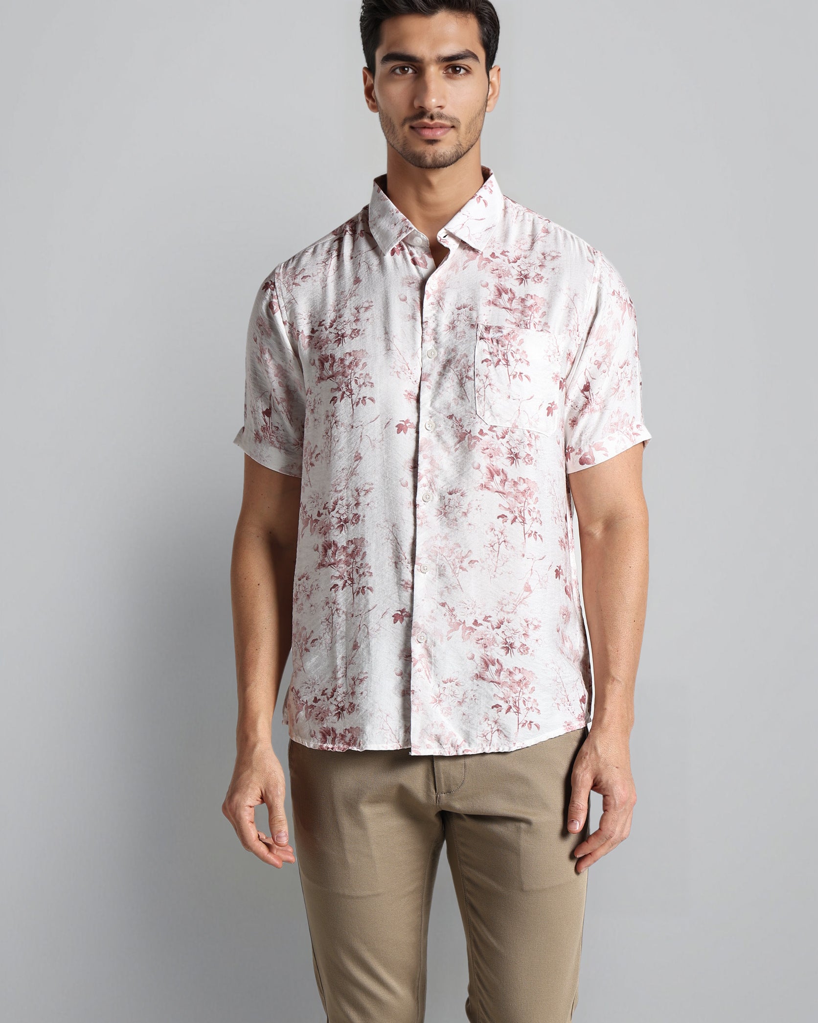 Man wearing a white patterned shirt and beige pants on a gray background