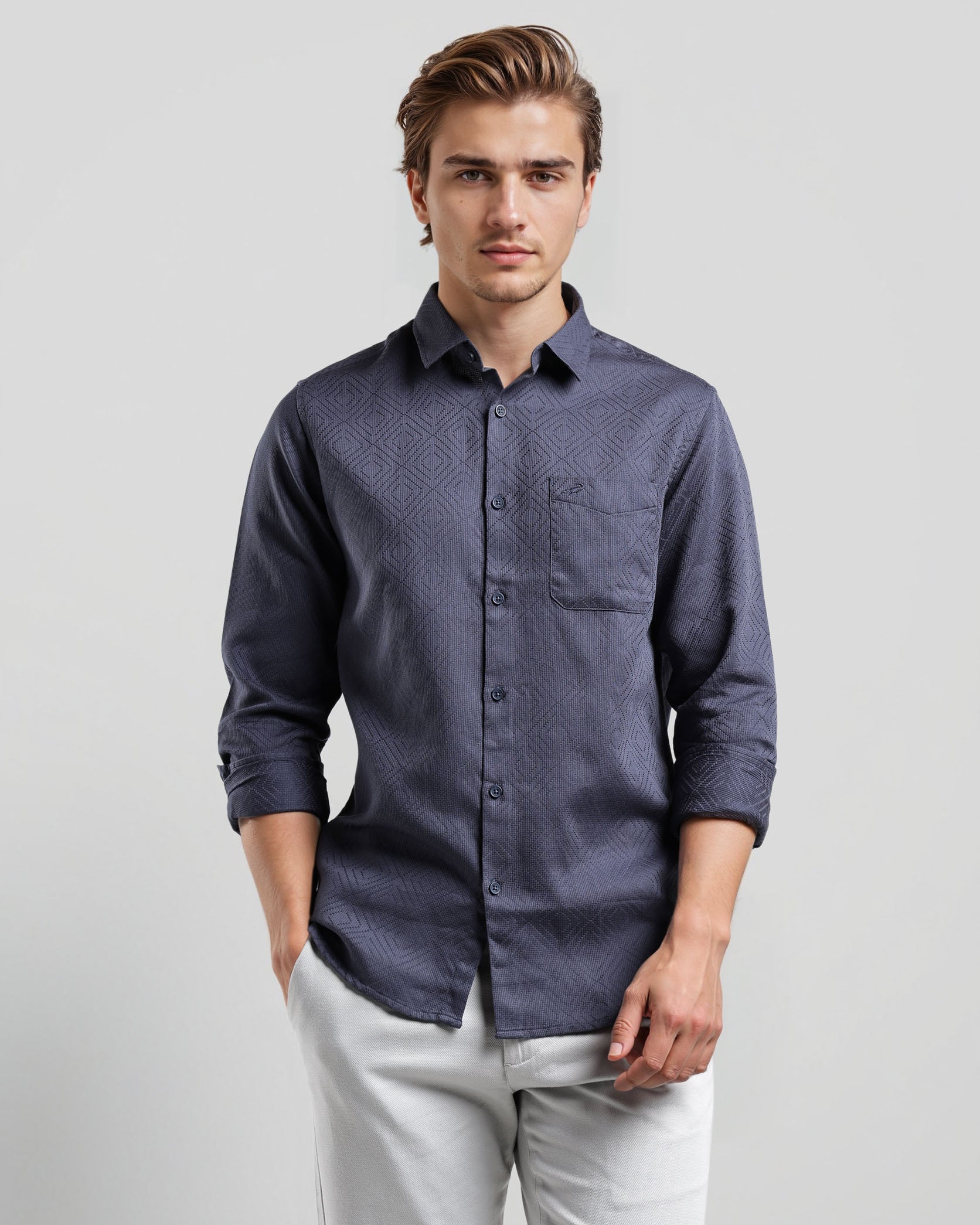 Man wearing a dark blue button-up shirt and light gray pants on a plain background