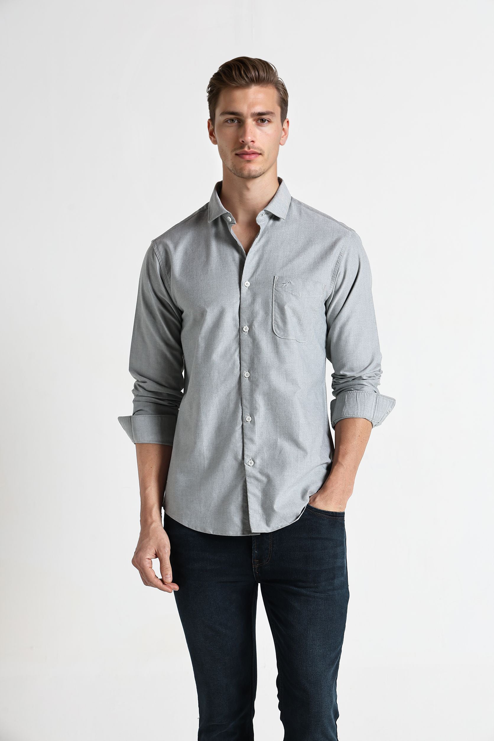 Man wearing a light gray button-up shirt and dark jeans on a white background