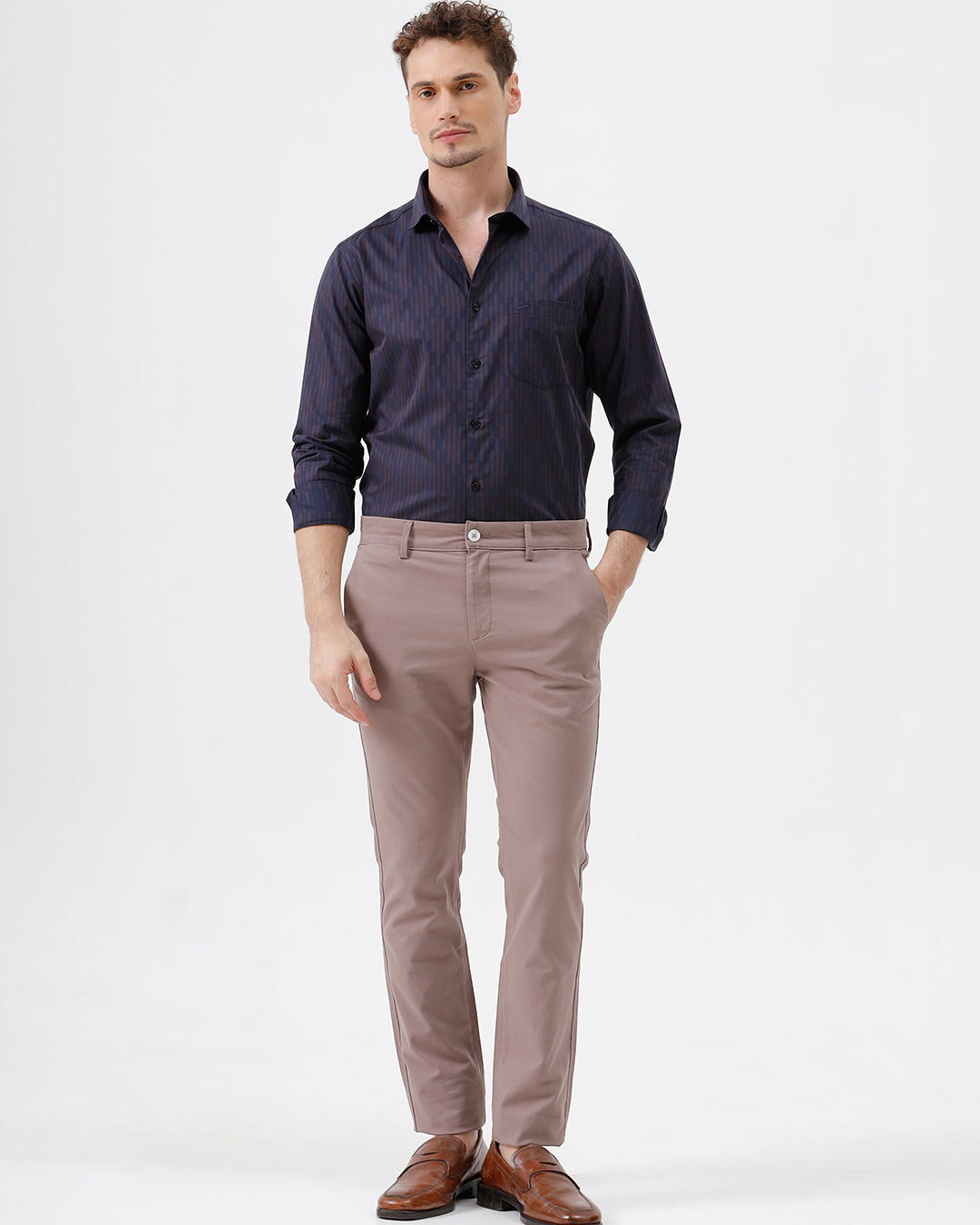 A man wearing a dark navy blue button-down shirt with thin vertical red stripes and light brown trousers, standing against a plain white studio background.