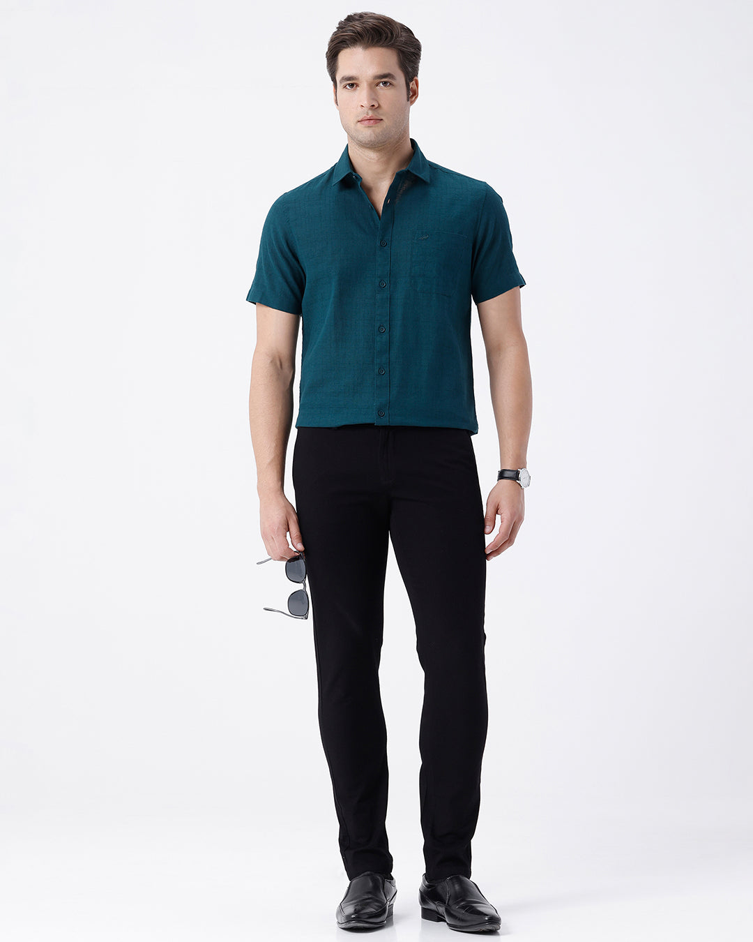 A man wearing slim-fit black trousers, a teal button-down shirt, and black leather dress shoes, standing against a plain white studio background.