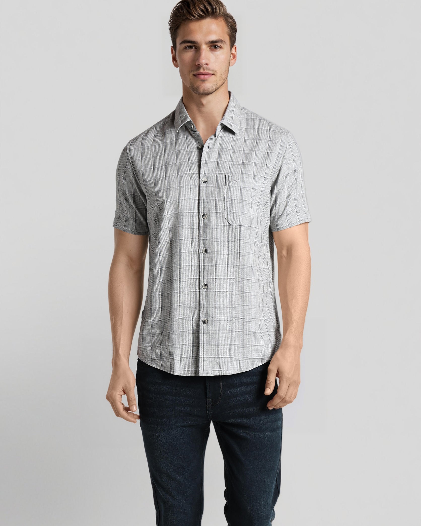 Man wearing a checkered short-sleeve shirt and dark pants on a light gray background