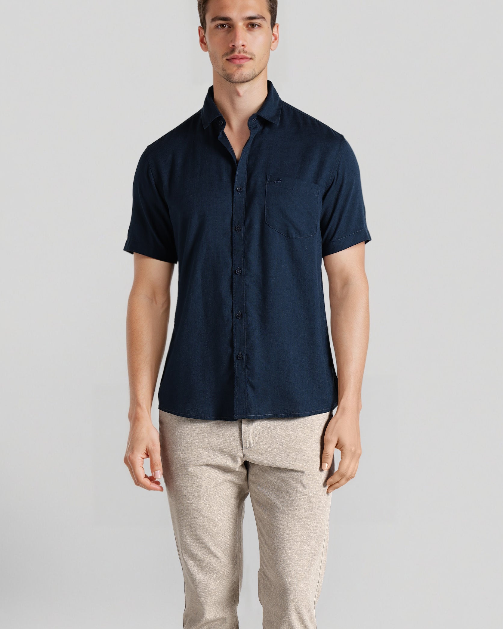 Man wearing a navy short-sleeve shirt and beige pants on a light gray background