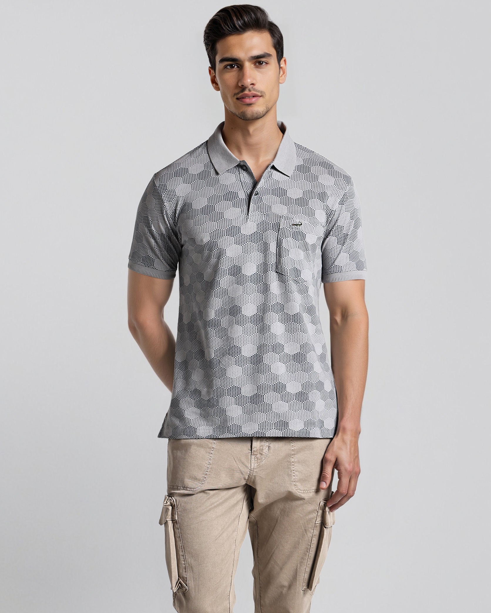 Man wearing a patterned gray polo shirt and beige pants on a light gray background