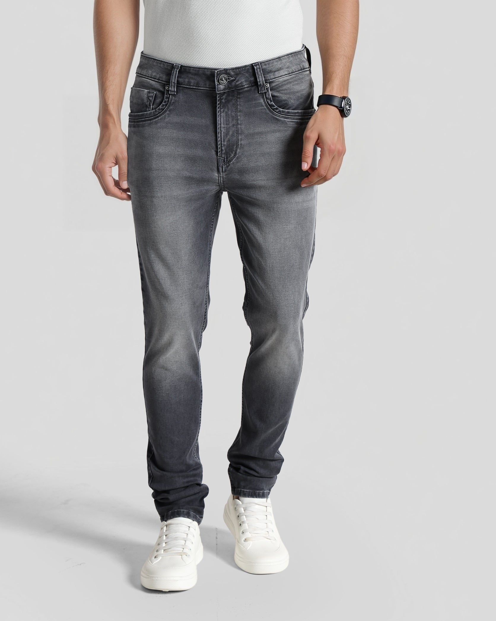 Person wearing gray jeans and white sneakers on a plain background