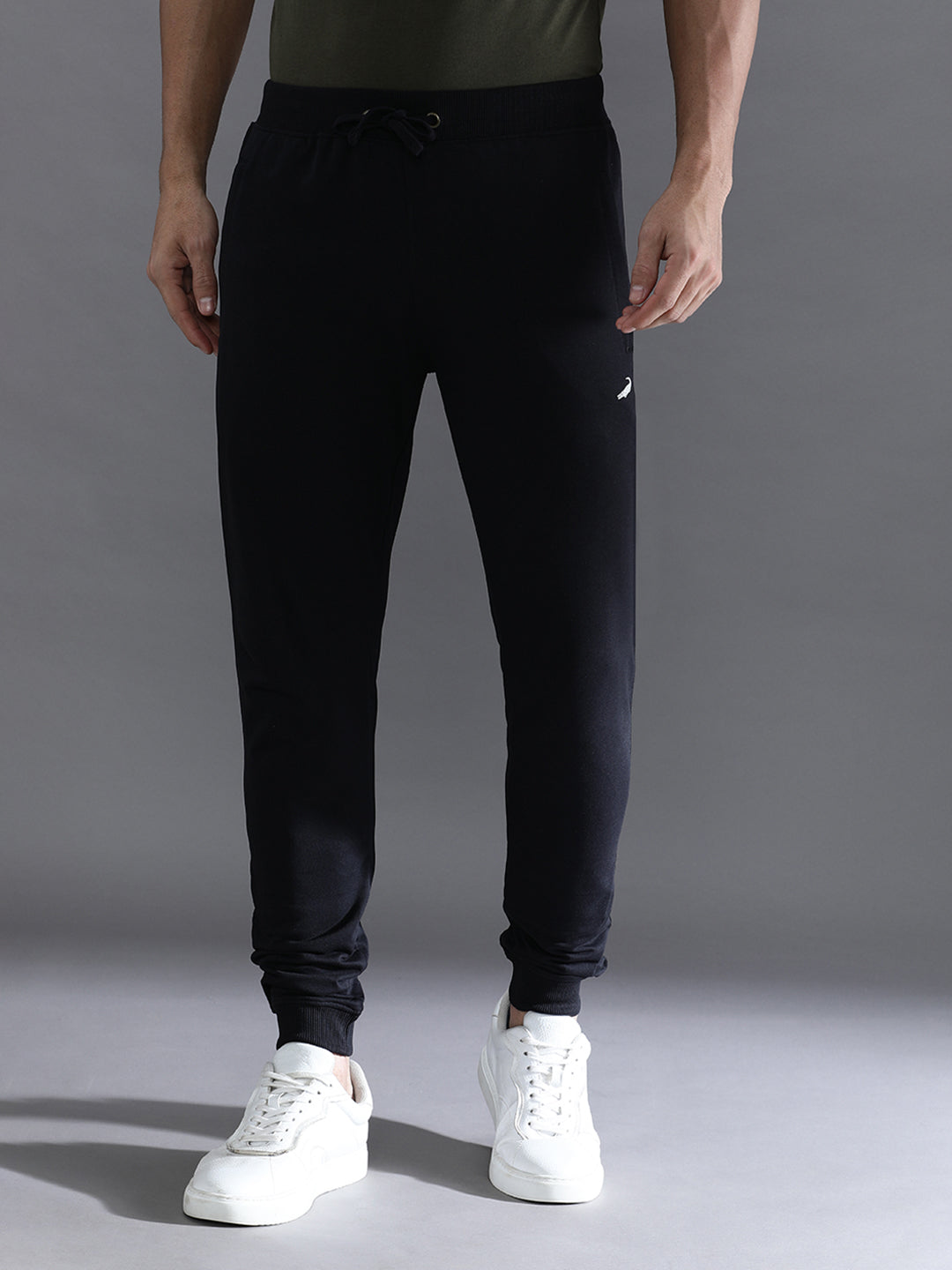 Person wearing black jogger pants and white sneakers on a gray background