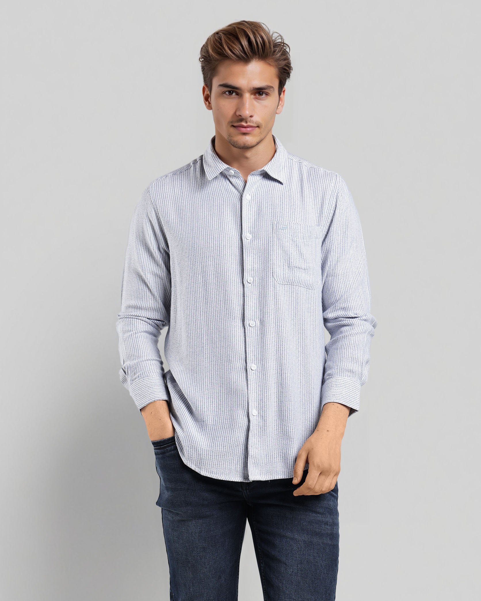 Man wearing a light blue striped shirt and dark jeans on a gray background