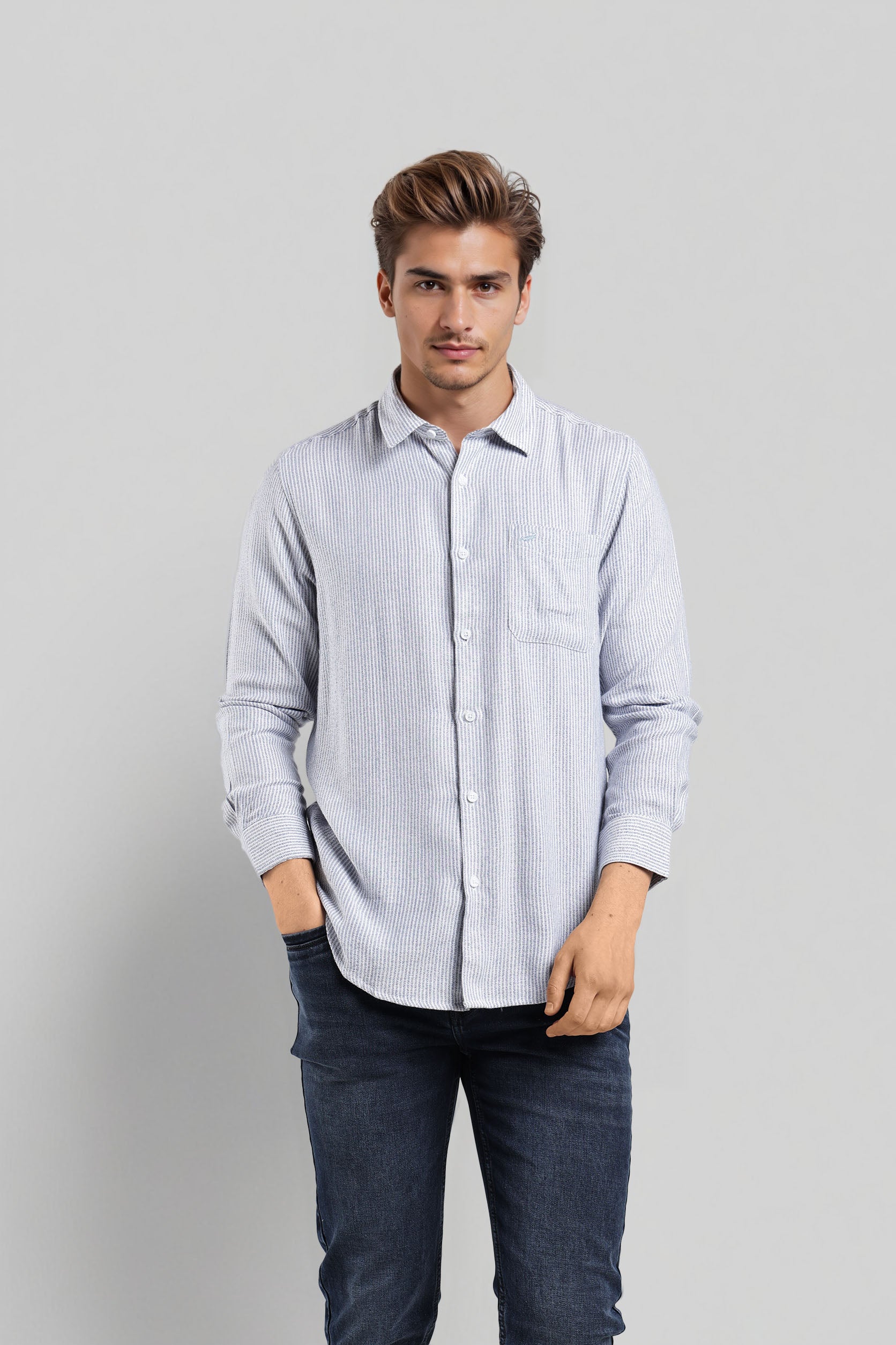 Man wearing a light blue striped shirt and dark jeans on a gray background