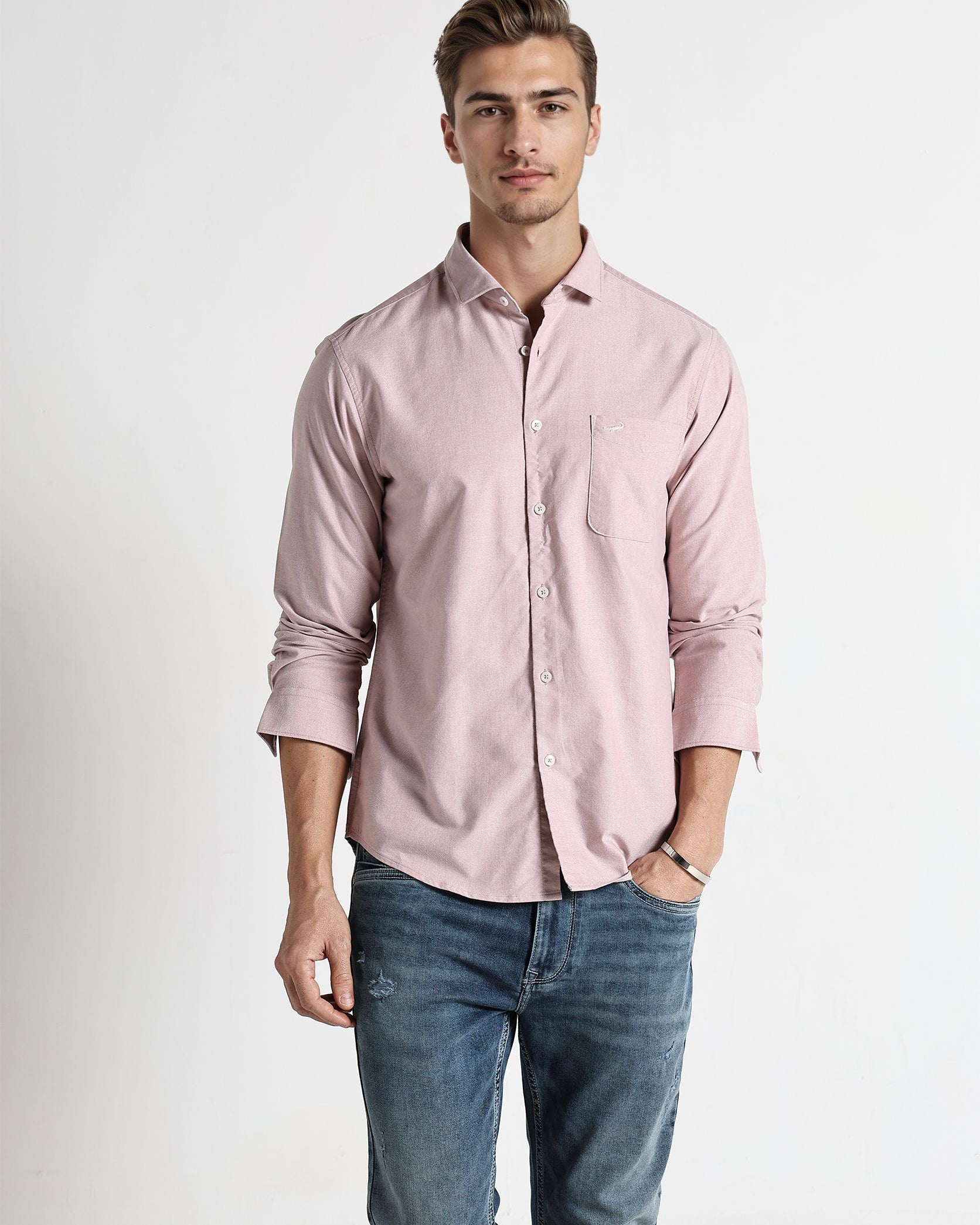 Man wearing a light pink shirt and blue jeans on a white background