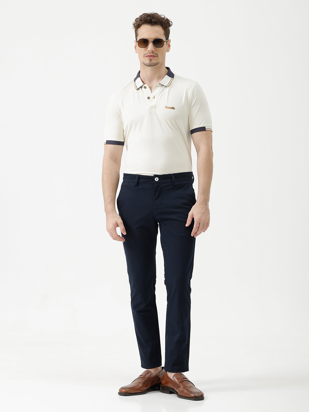 A man wearing a short-sleeve polo shirt in off-white with navy blue and gold trim on the collar and sleeve cuffs, paired with dark navy trousers, against a plain light gray background.